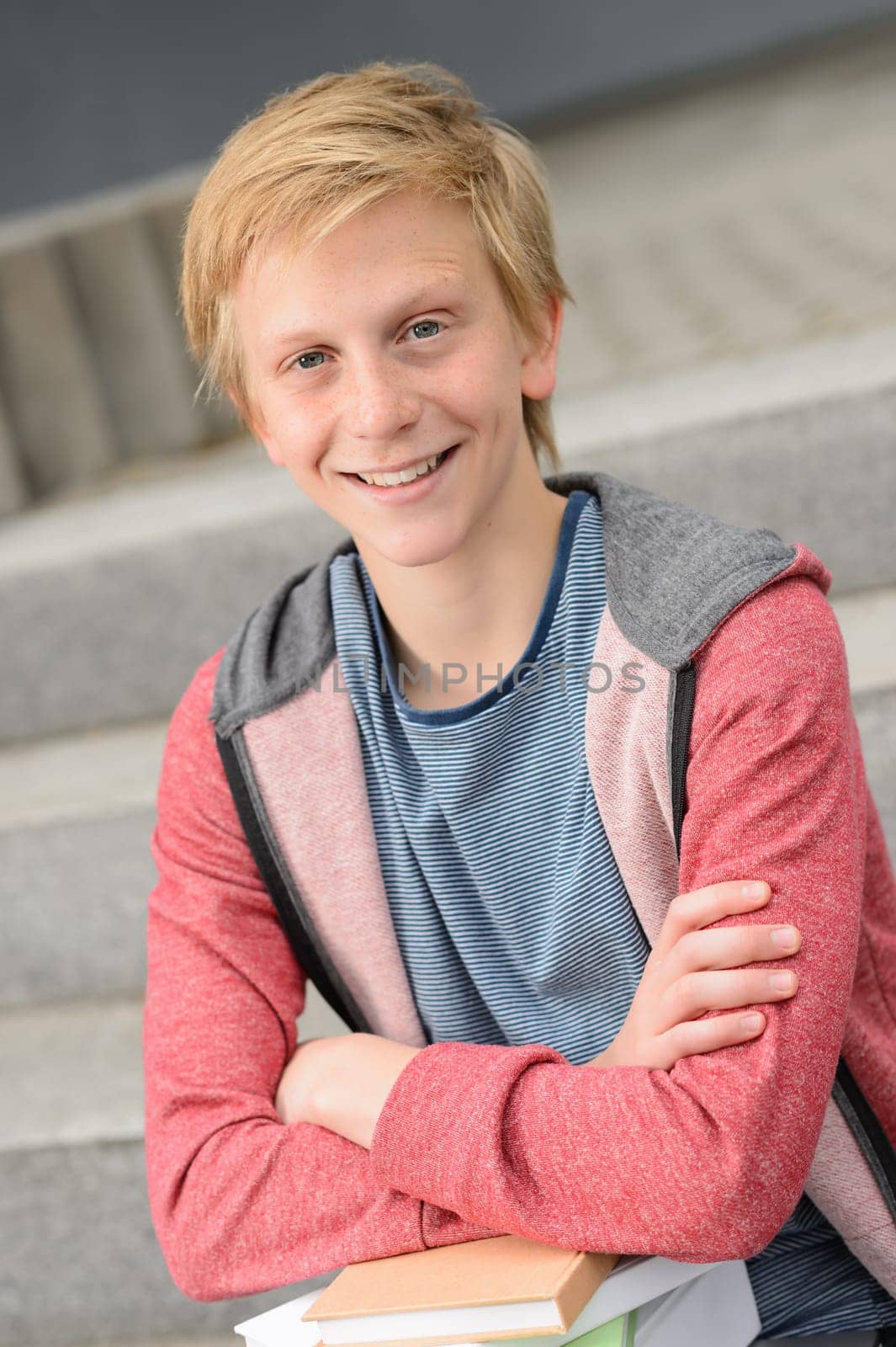 Smiling teenage student boy with books sitting outside on steps