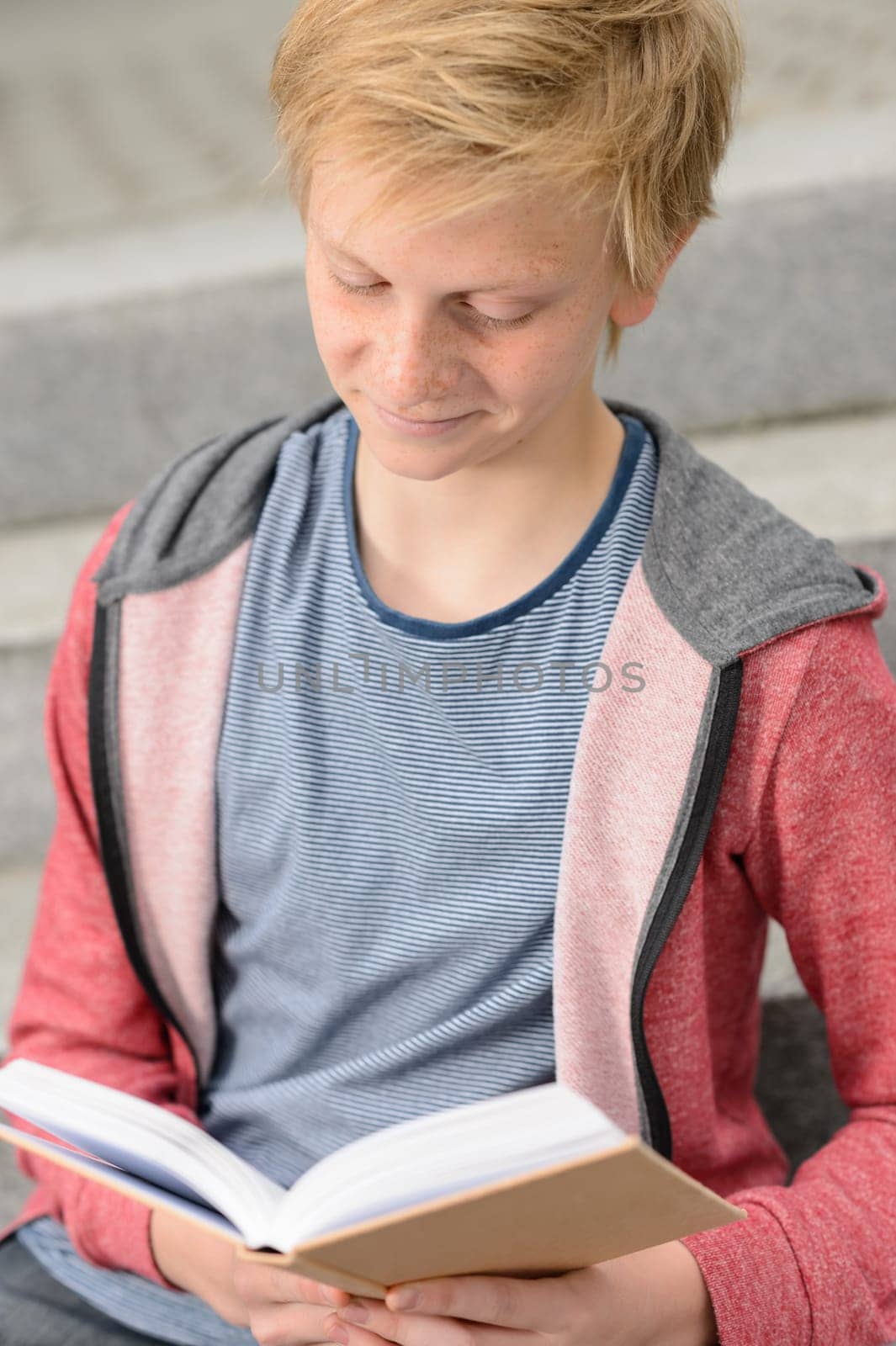Teenage boy studying reading book while sitting on school steps