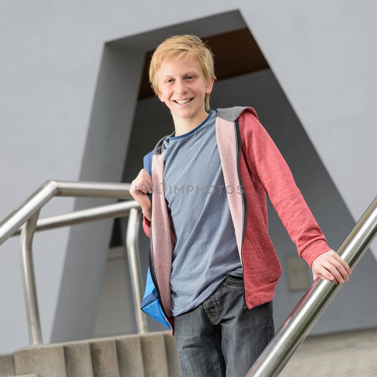 Happy teenage student boy standing on steps outside his school