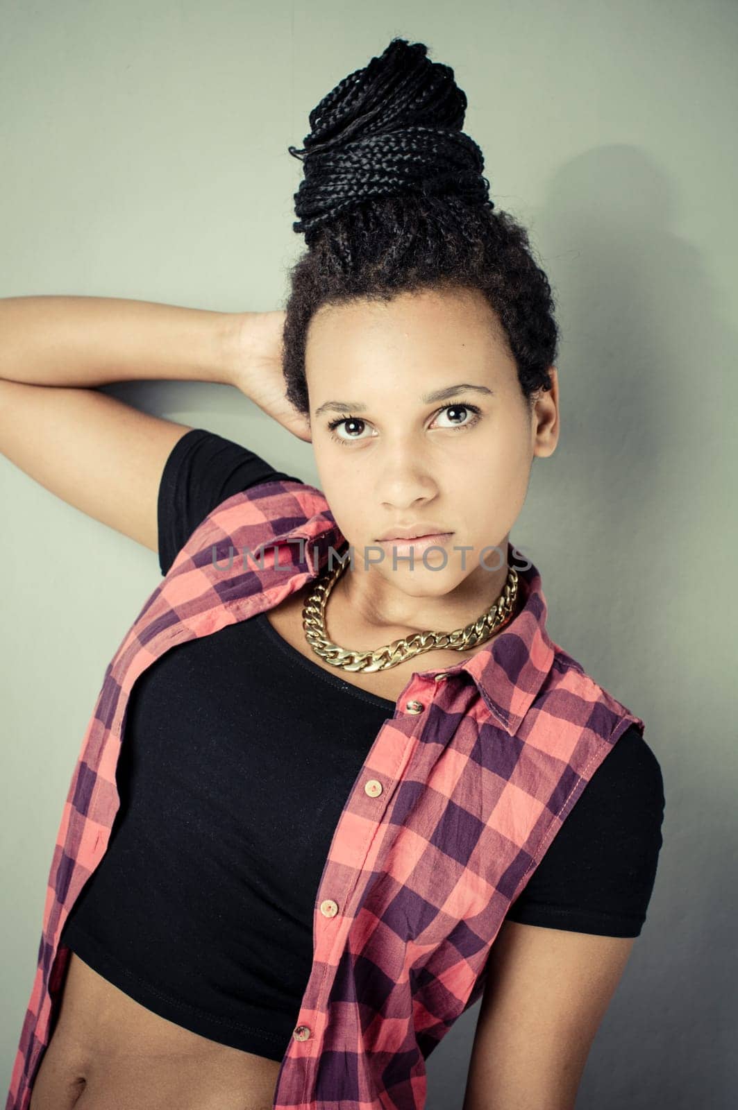 Young african girl with black dreadlocks wearing trendy hip-hop fashion and posing in front of a grey wall.