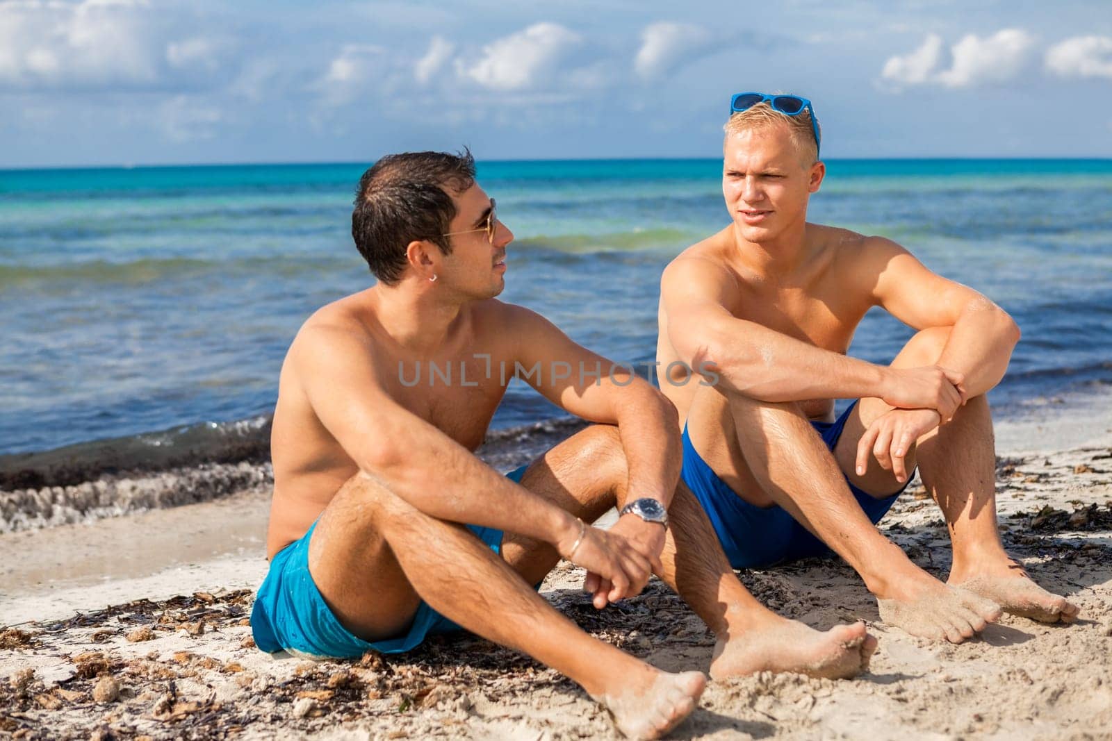 Two young men friends relax in the sand while on holiday on the beach in summer