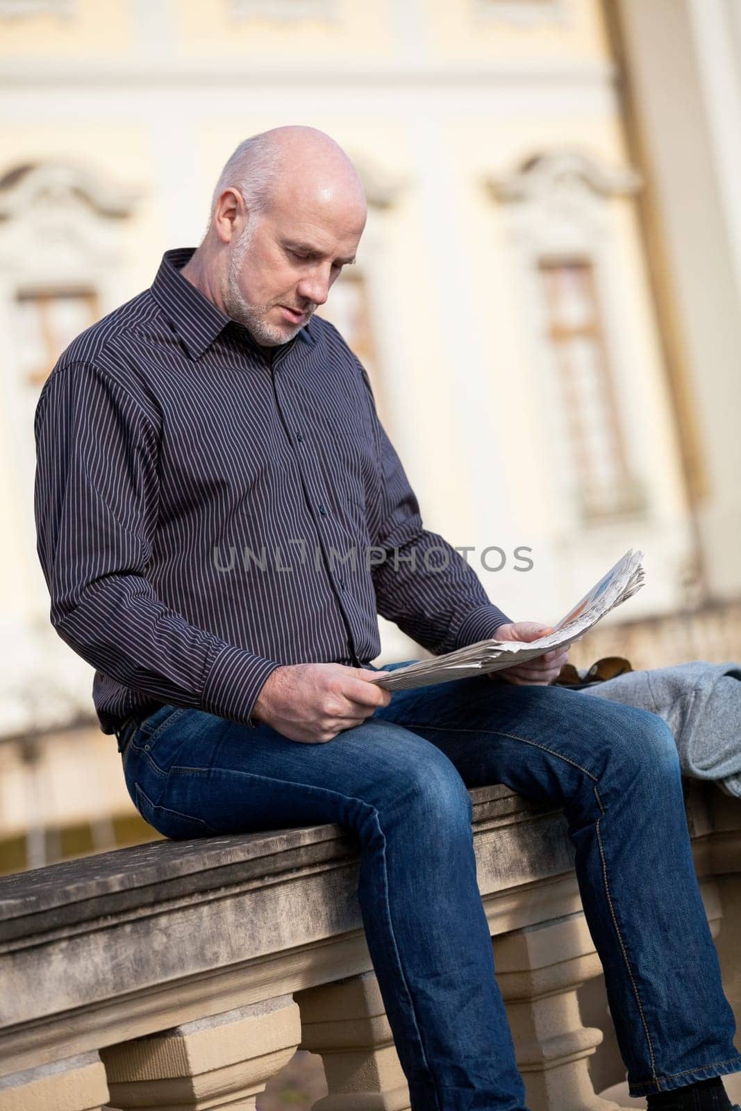 adult older man sitting outdoors reads a newspaper news free time