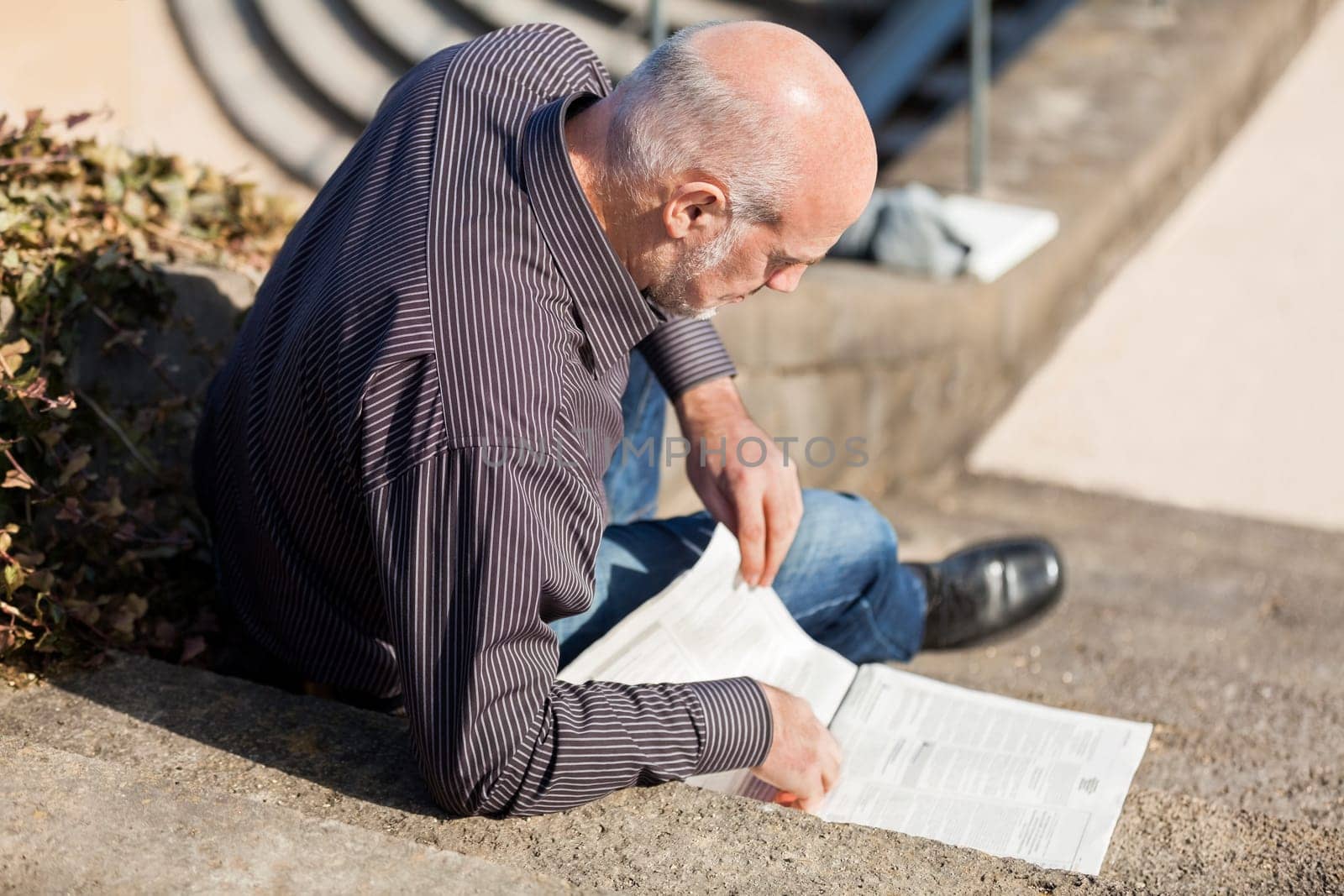 Middle-aged man,senior sitting with a newspaper on a staircase in spring outdoors