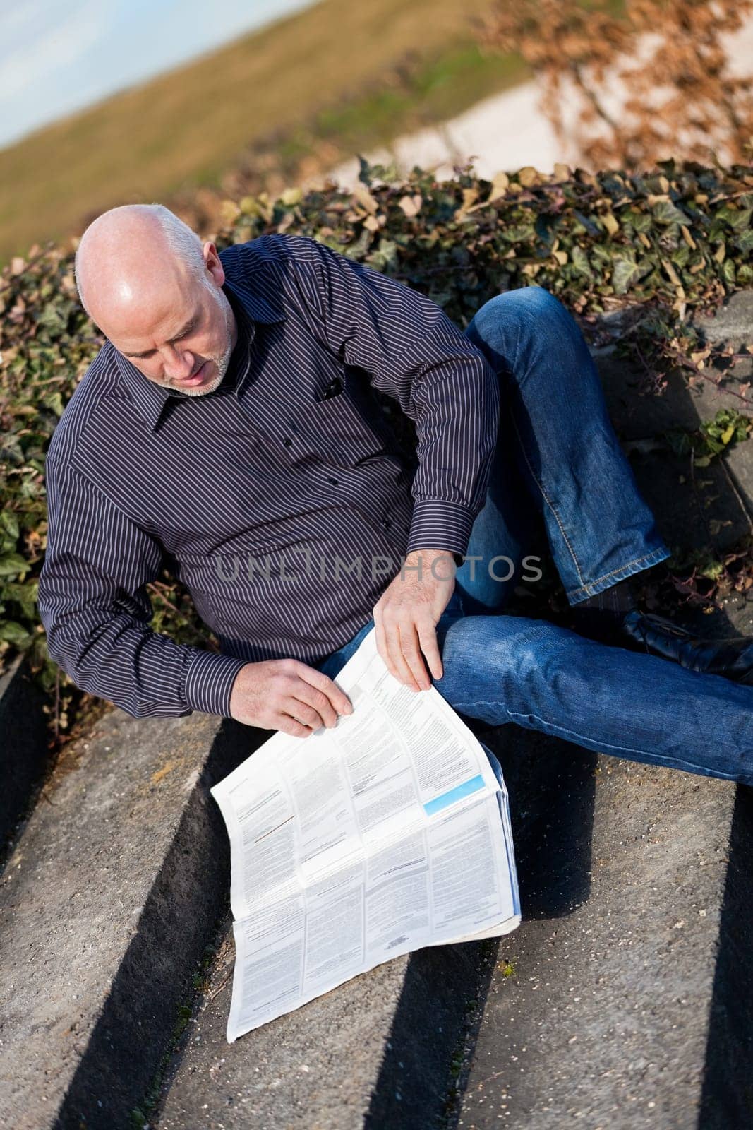 Middle-aged man,senior sitting with a newspaper on a staircase in spring outdoors