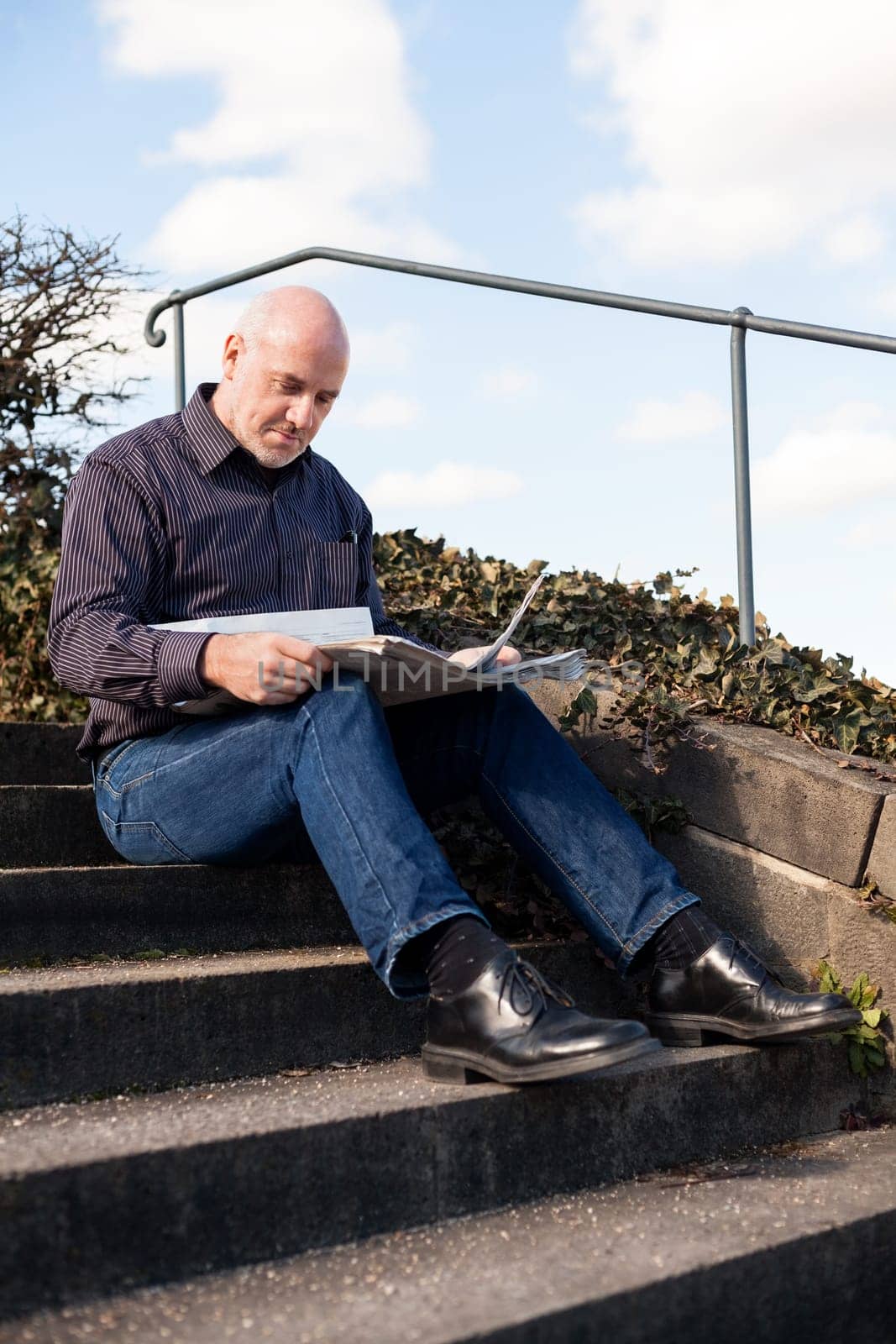 Middle-aged man,senior sitting with a newspaper on a staircase in spring outdoors