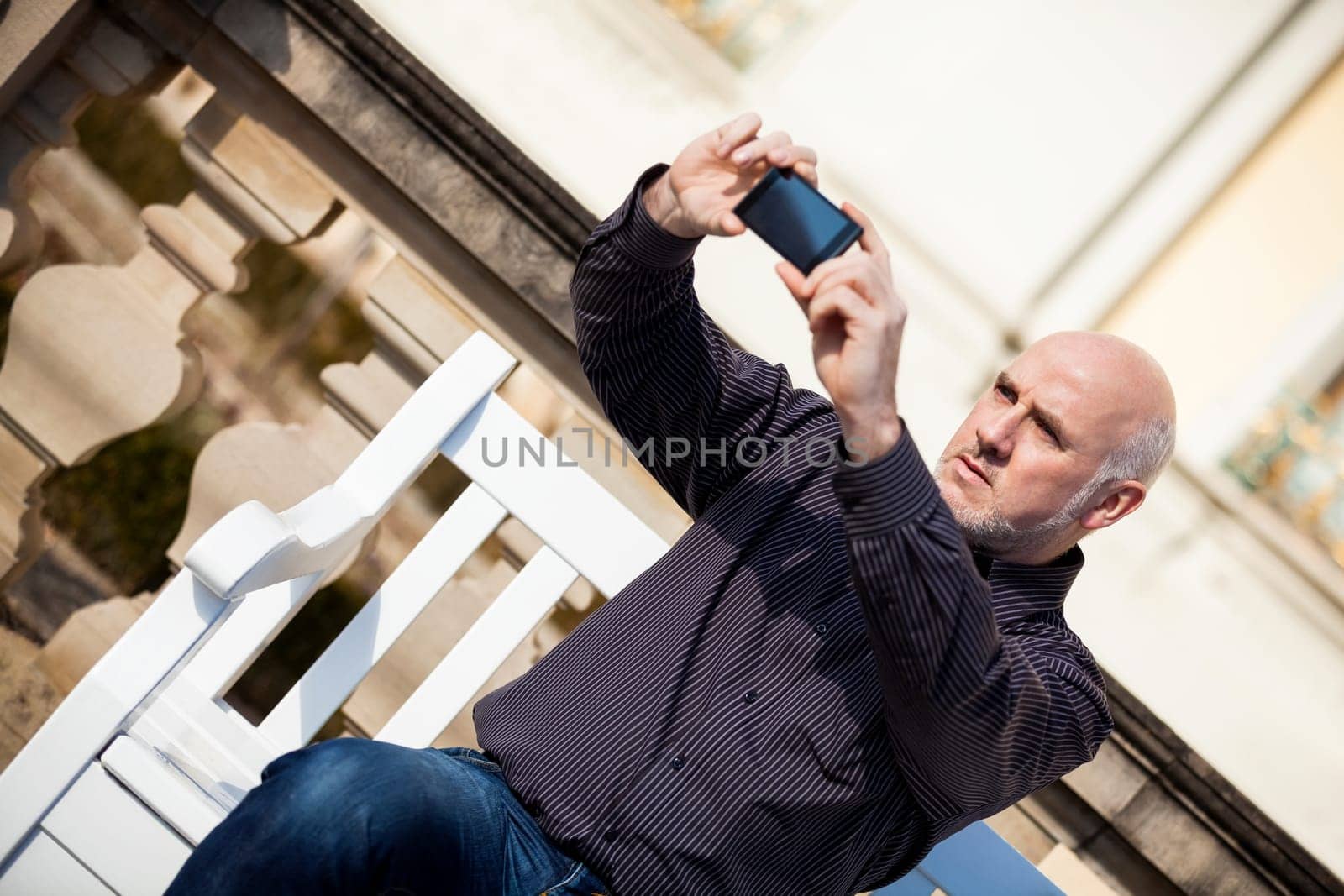 Attractive older man senior photographs himself with his mobile phone smartphone in the park
