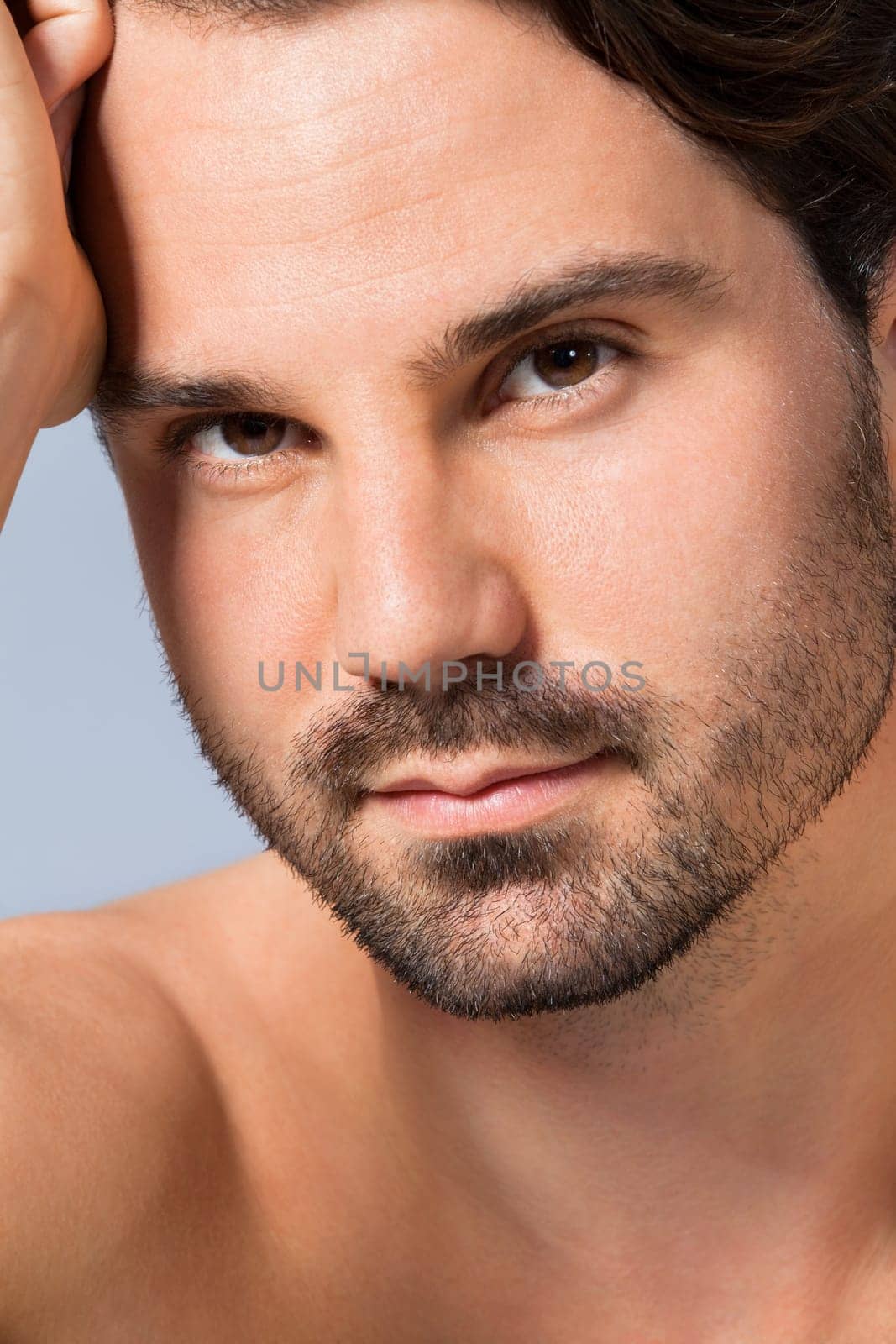 Young naked man with dark hair and beard as a portrait against a grey background