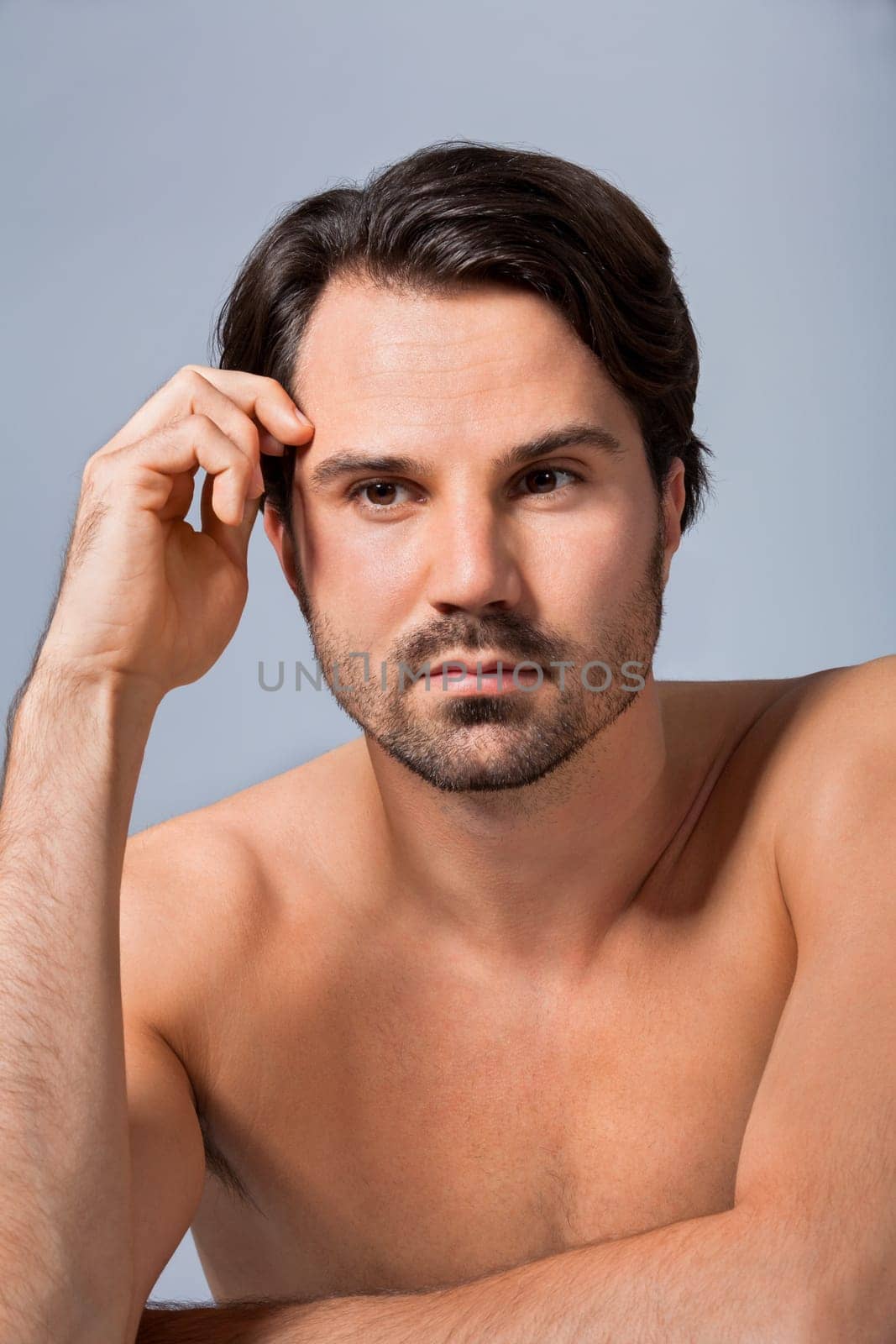 Young naked man with dark hair and beard as a portrait against a grey background