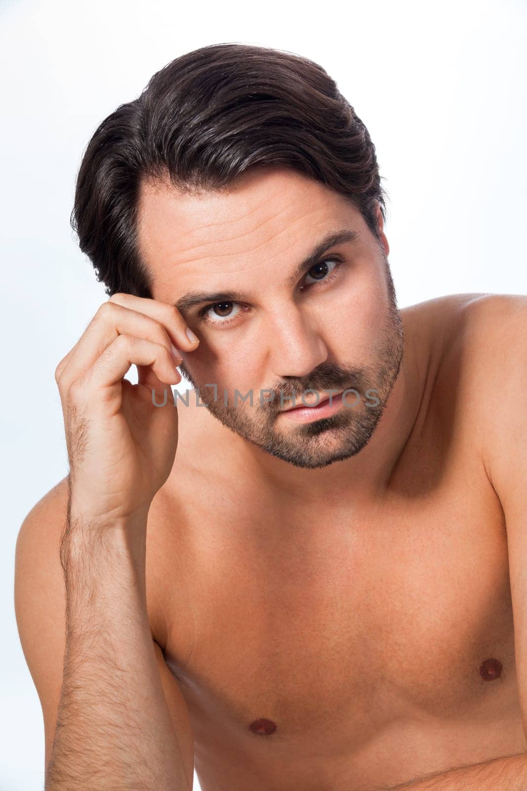 Young naked man with dark hair and beard as a portrait against a grey background