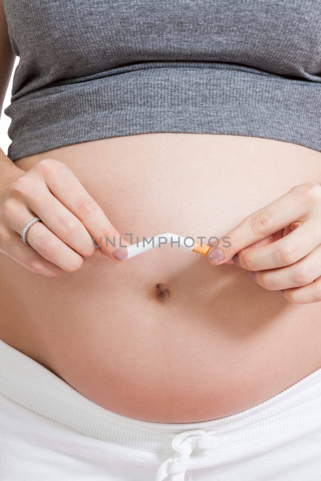 Pregnant woman breaks a cigarette in front of her baby belly isolated against white background