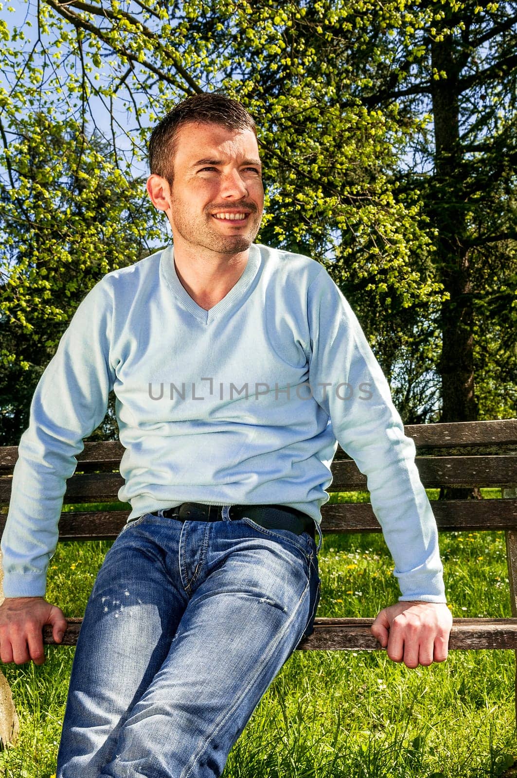 attractive man is relaxing on a bench in a natural environement