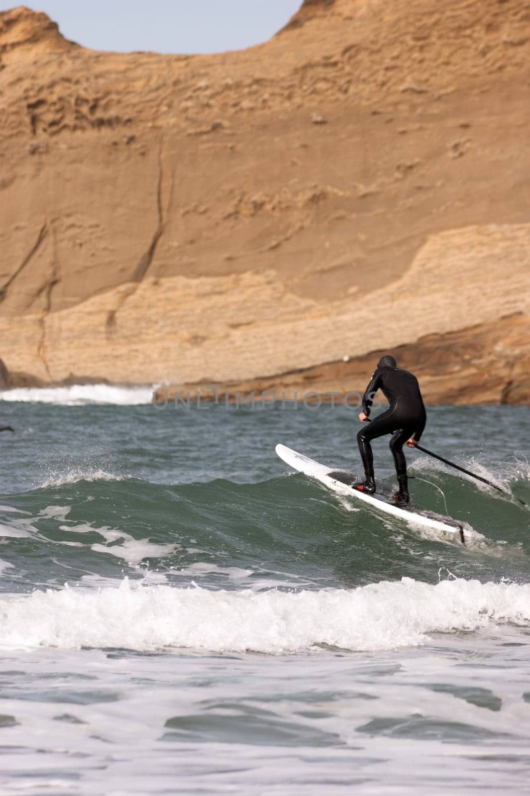 One man paddles out into the ocean on long paddle board near rock formation