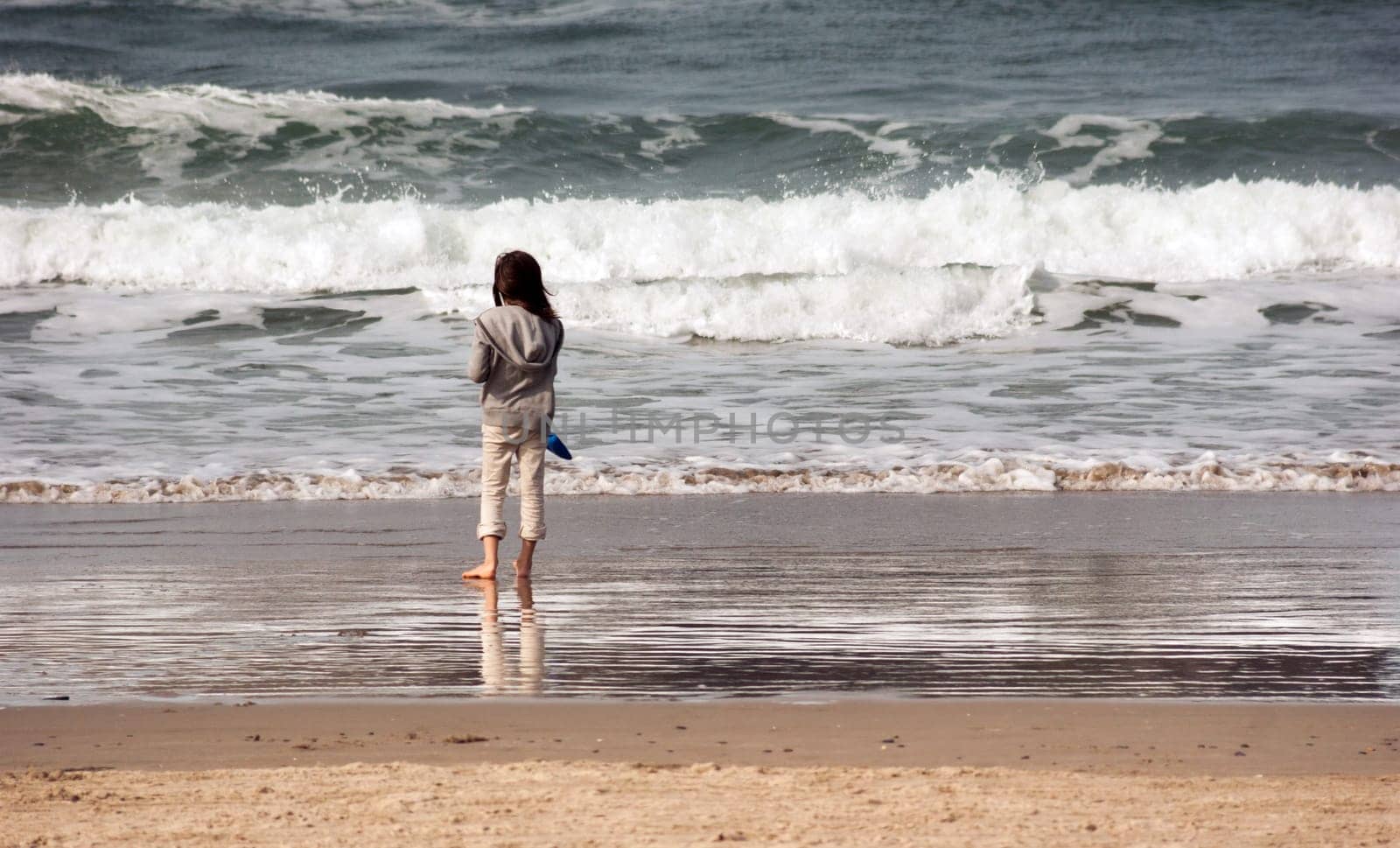 Young girl stands for a moment looking out at the ocean waves crashing in