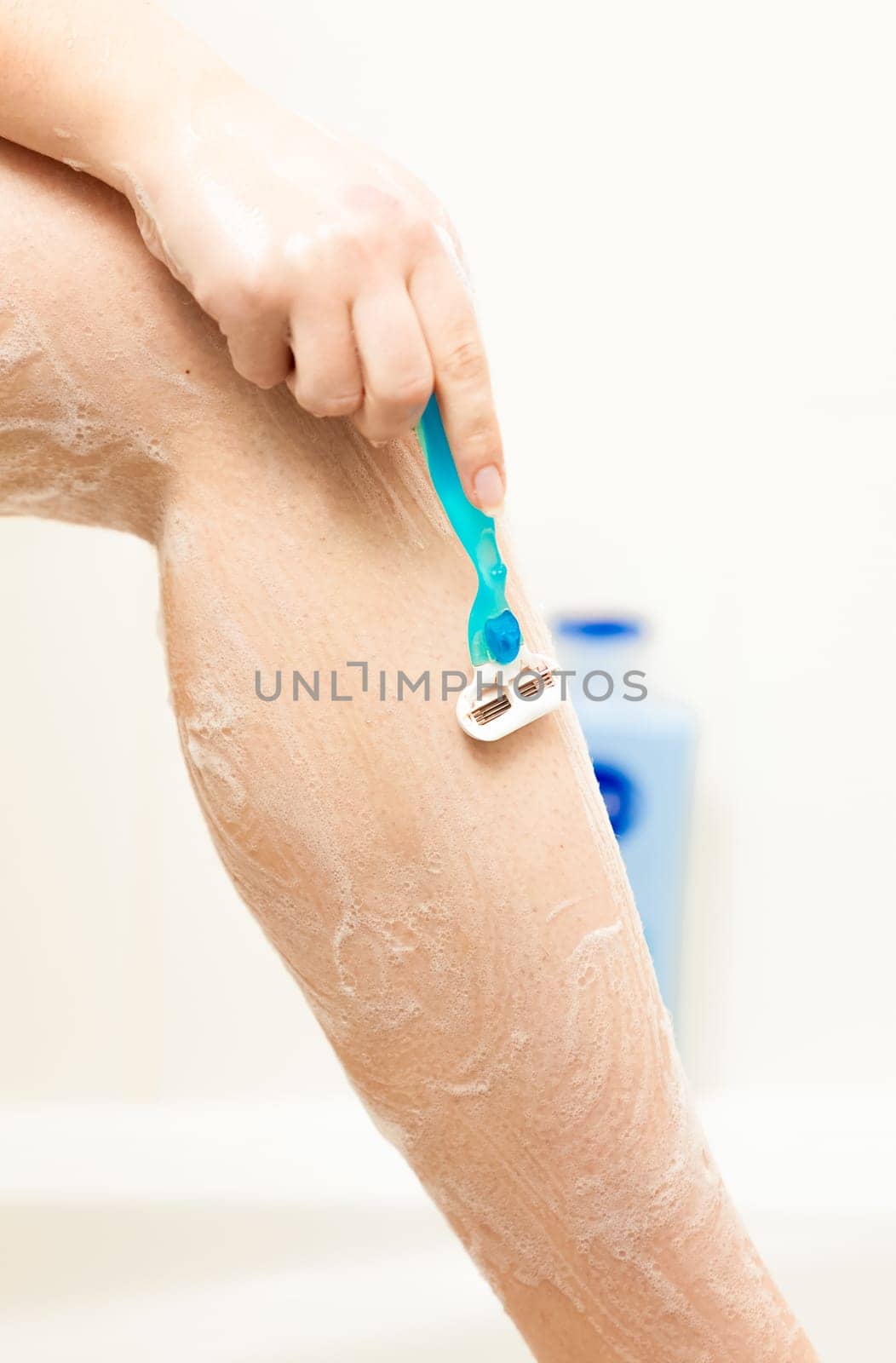 Closeup photo of woman shaving leg with blue razor