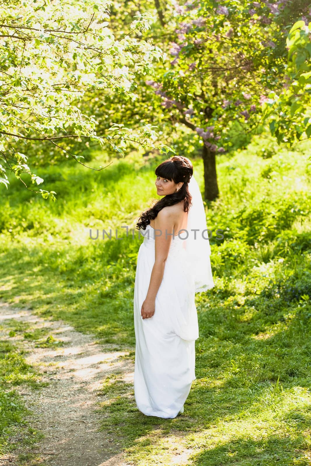 Beautiful brunette bride walking on path under trees at park
