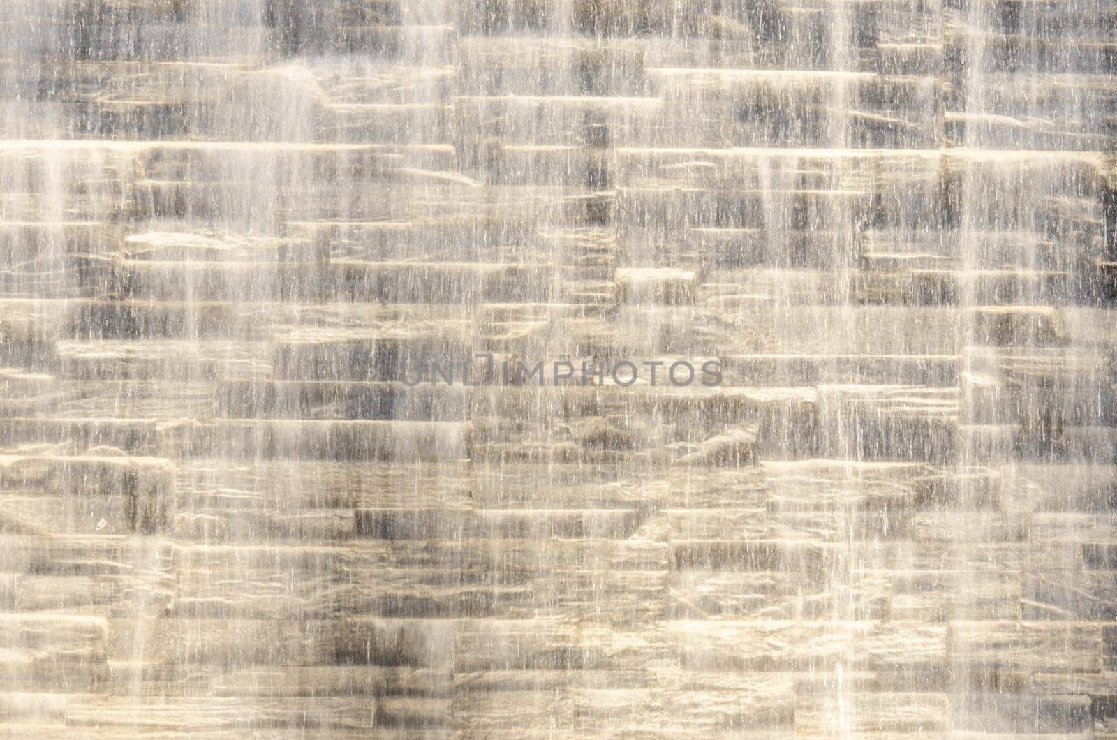 Falling water stream against stone wall rough texture with night backlight