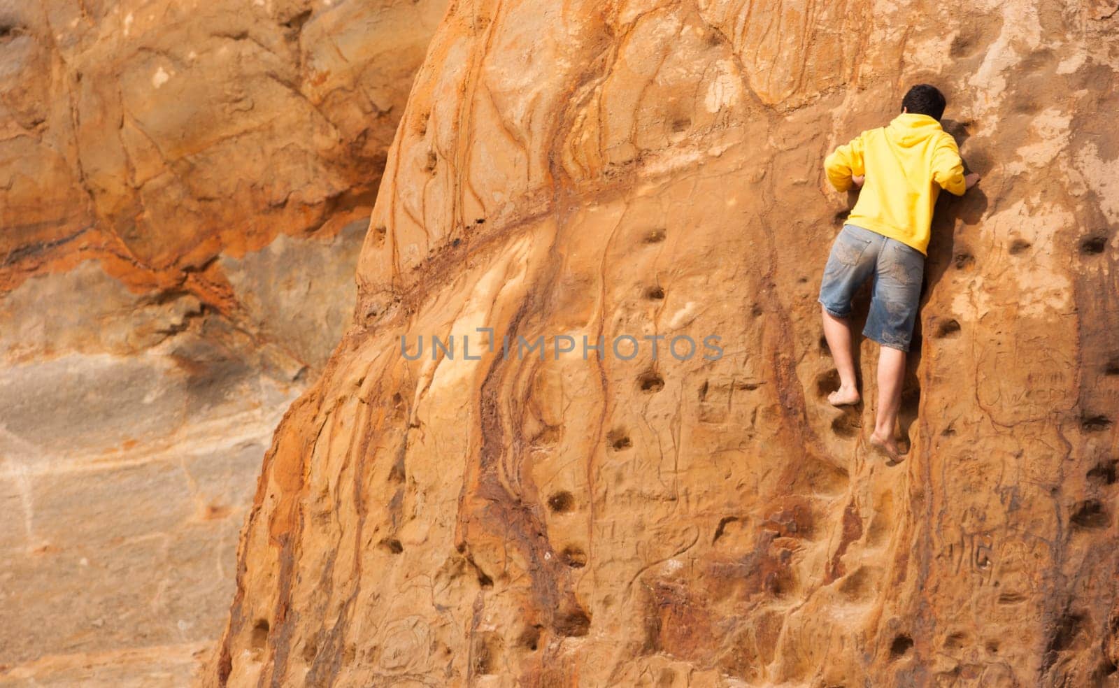 Young man in shorts and yellow sweatshirt climbing sandstone wall