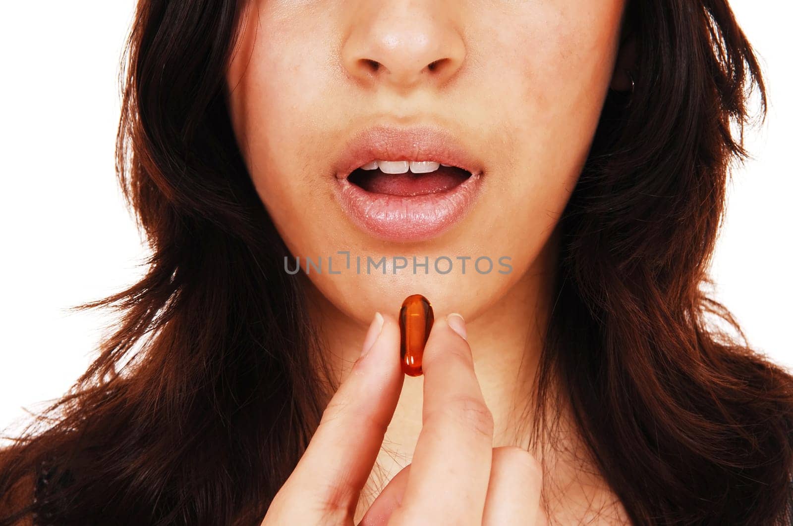 A closeup picture of the face on a young woman with an open mouth.taking a vitamin capsule, isolated on white background..