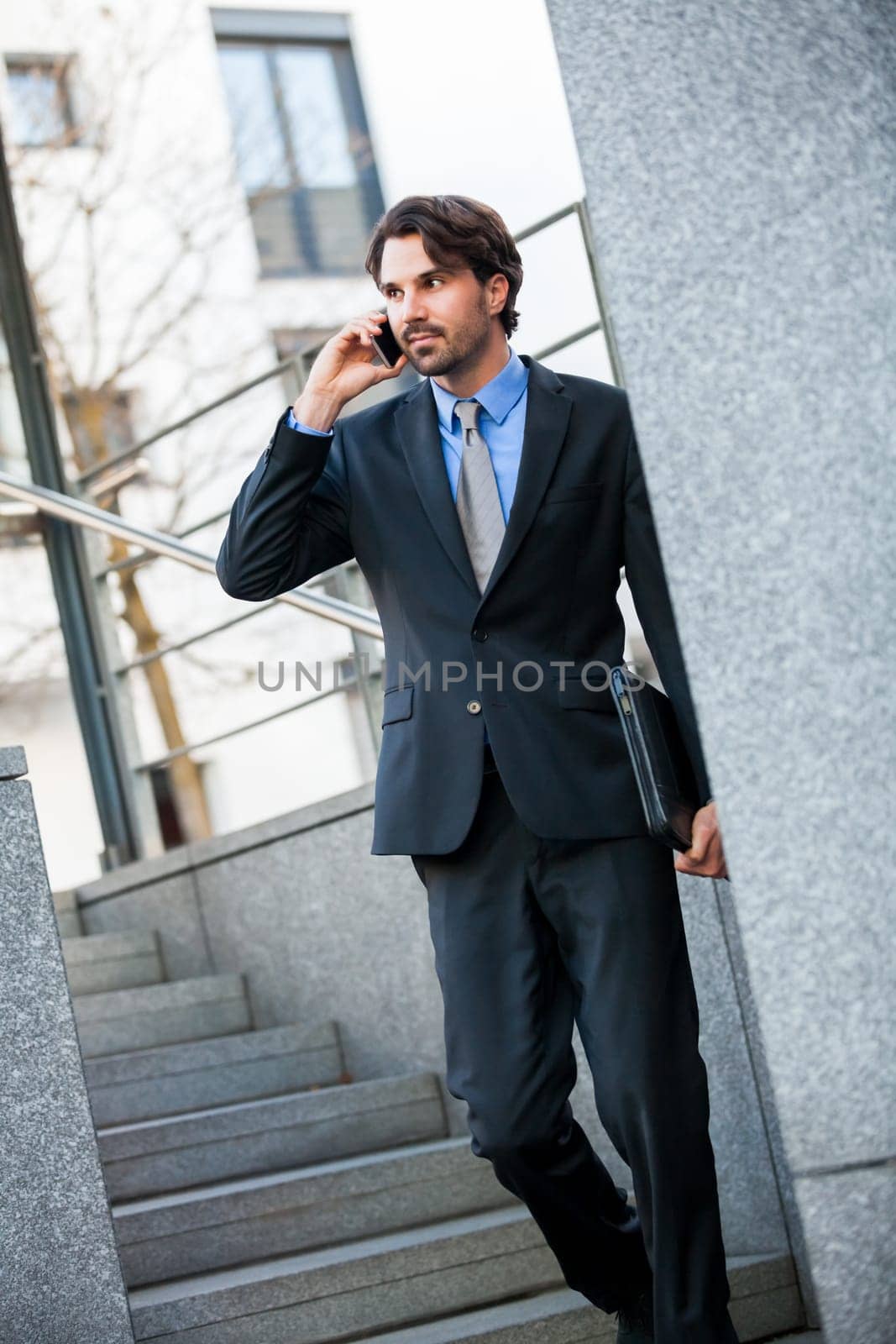 Young trendy successful businessman with mobile phone smartphone cheerful lyrane in front of an outdoor business building