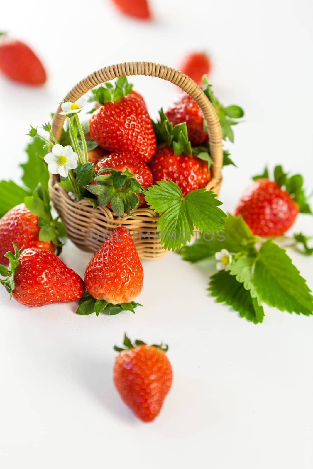 Fresh strawberries in a small basket with green leaves on a white background