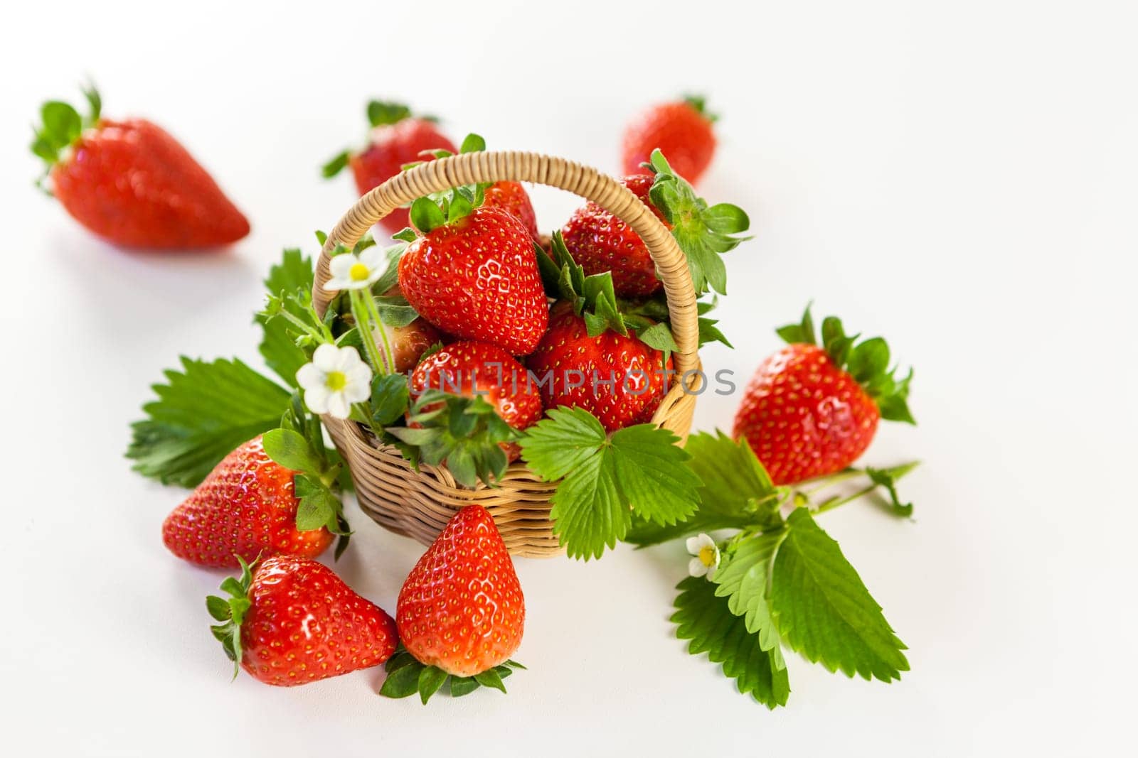 Fresh strawberries in a small basket with green leaves on a white background