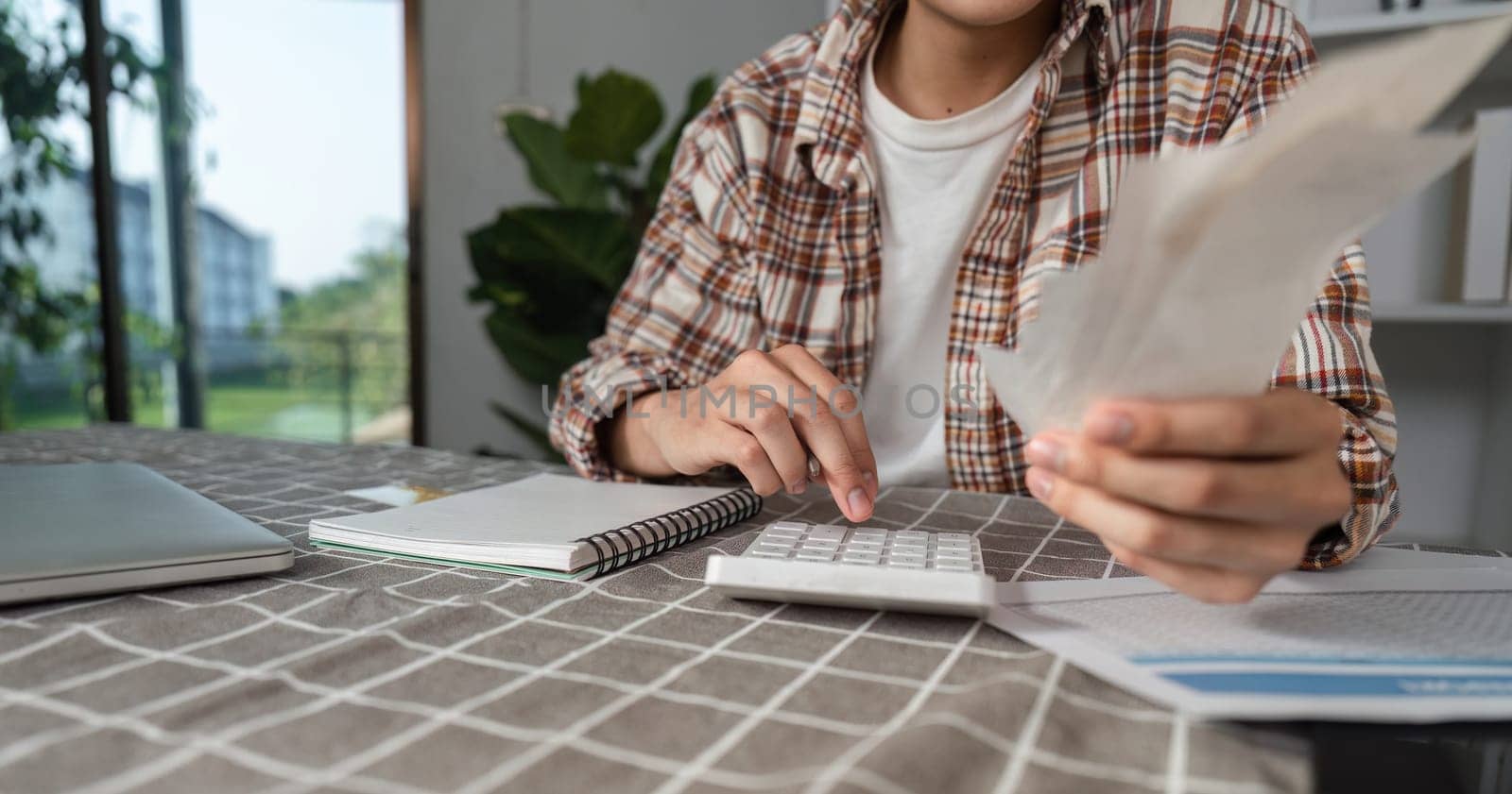 A young man reviews cash and uses a calculator for budgeting at home, emphasizing financial management and planning.