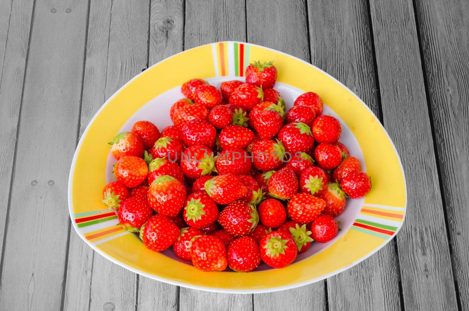 Plate of strawberries stands on a weathered wooden board