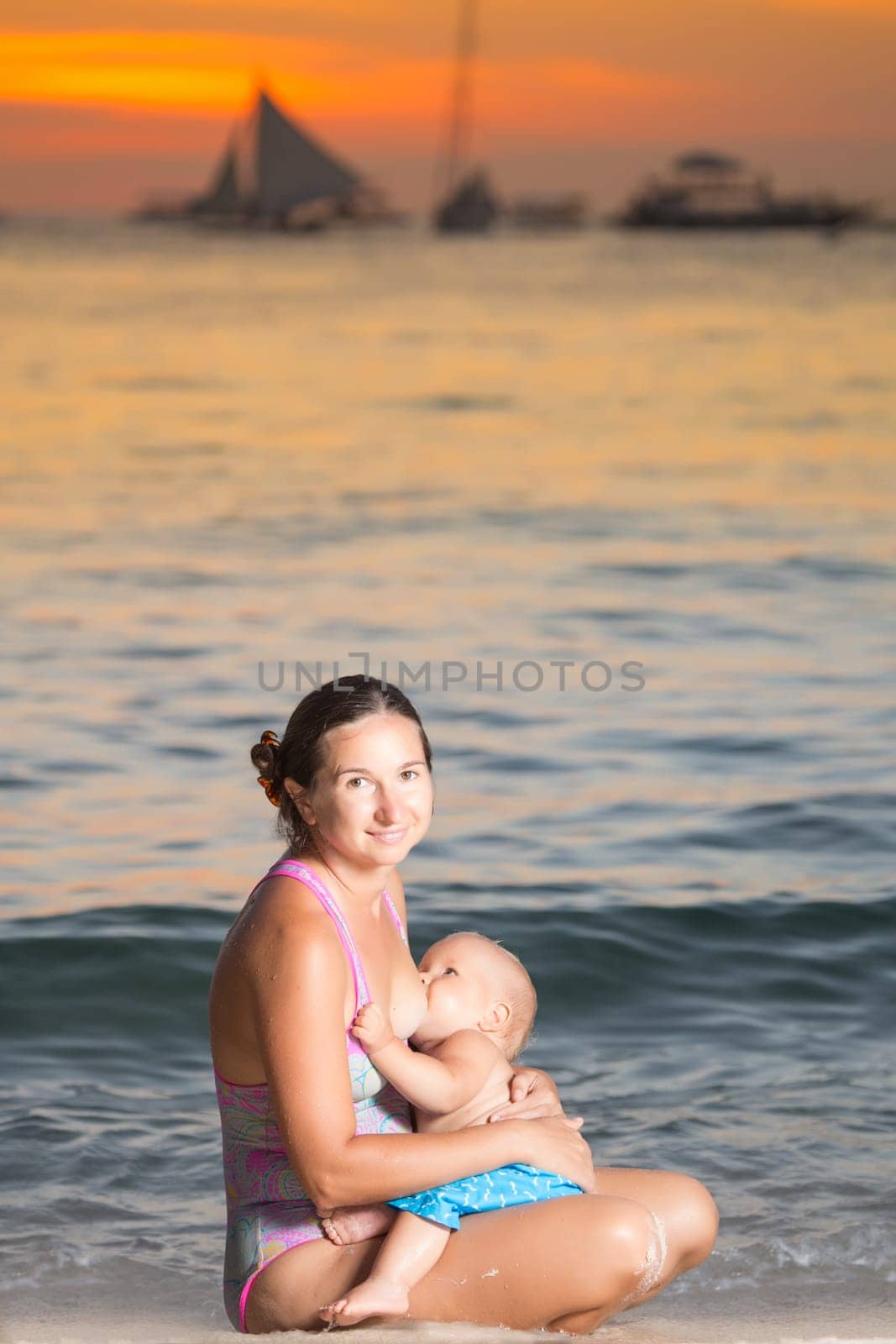 Mother breastfeeding baby on the beach at sunset