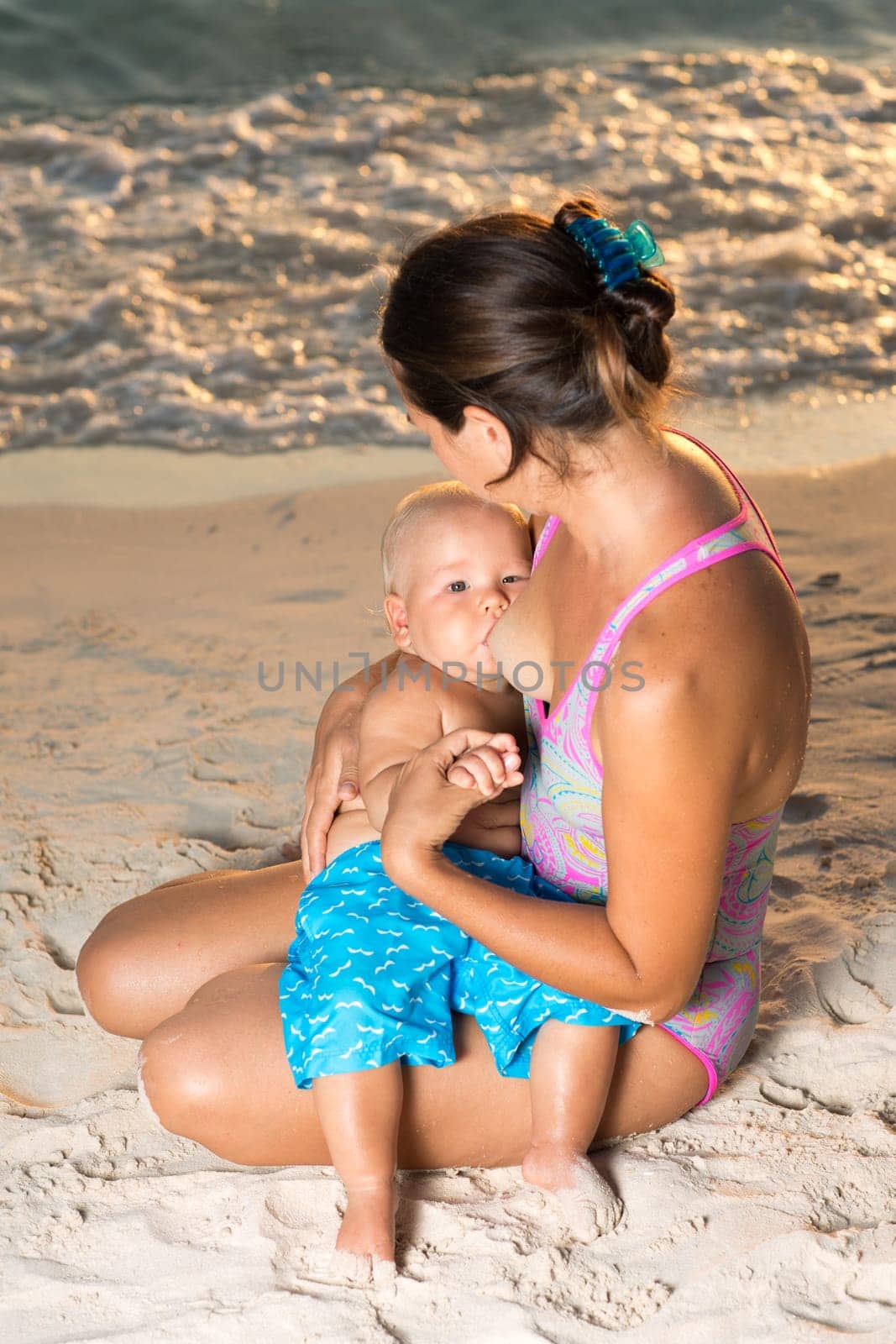 Mother breastfeeding baby on the beach at sunset