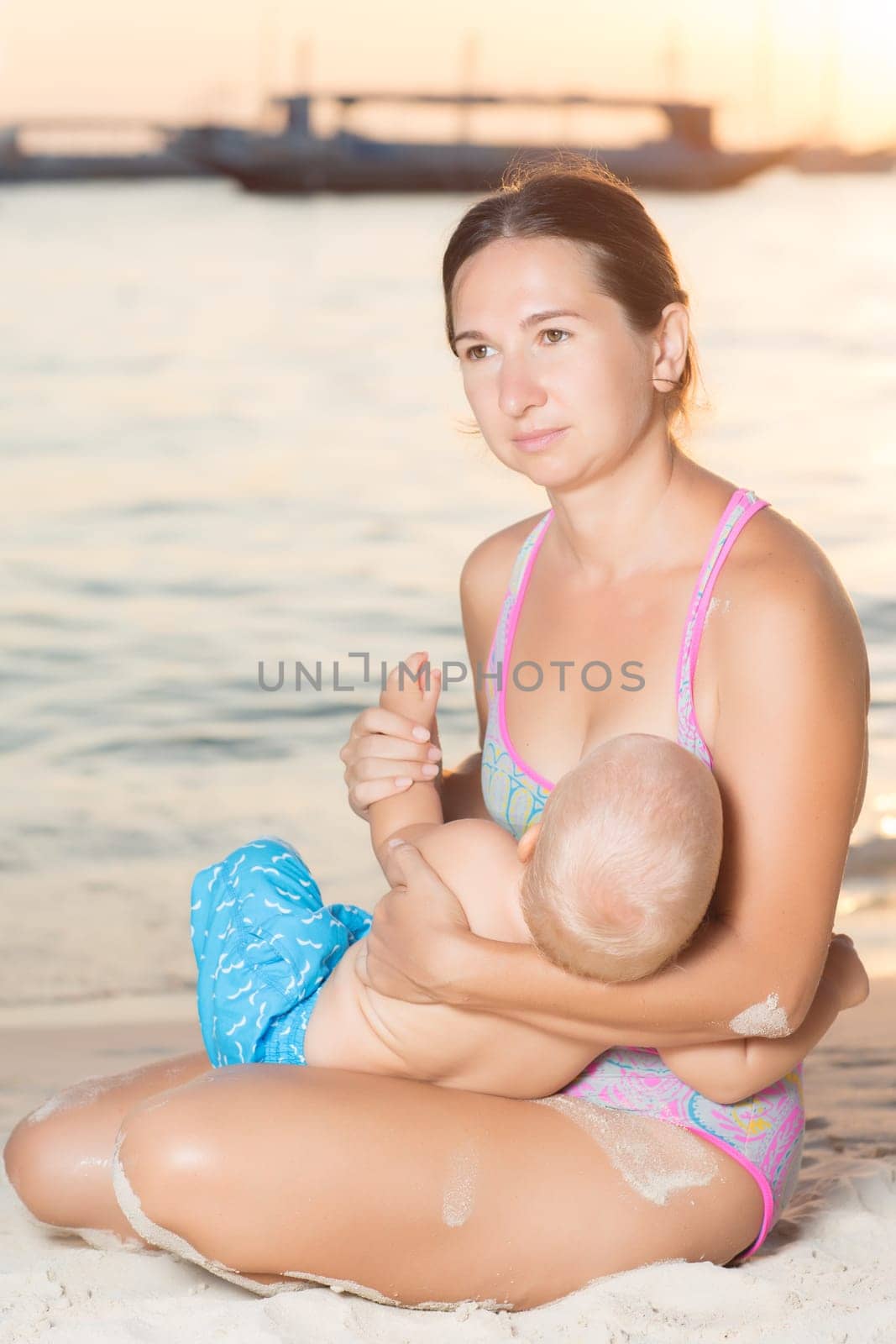 Mother breastfeeding baby on the beach at sunset