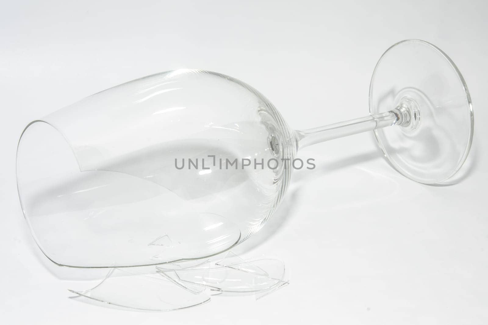 Shattered broken-down wine glass with sharp shards lying on white background