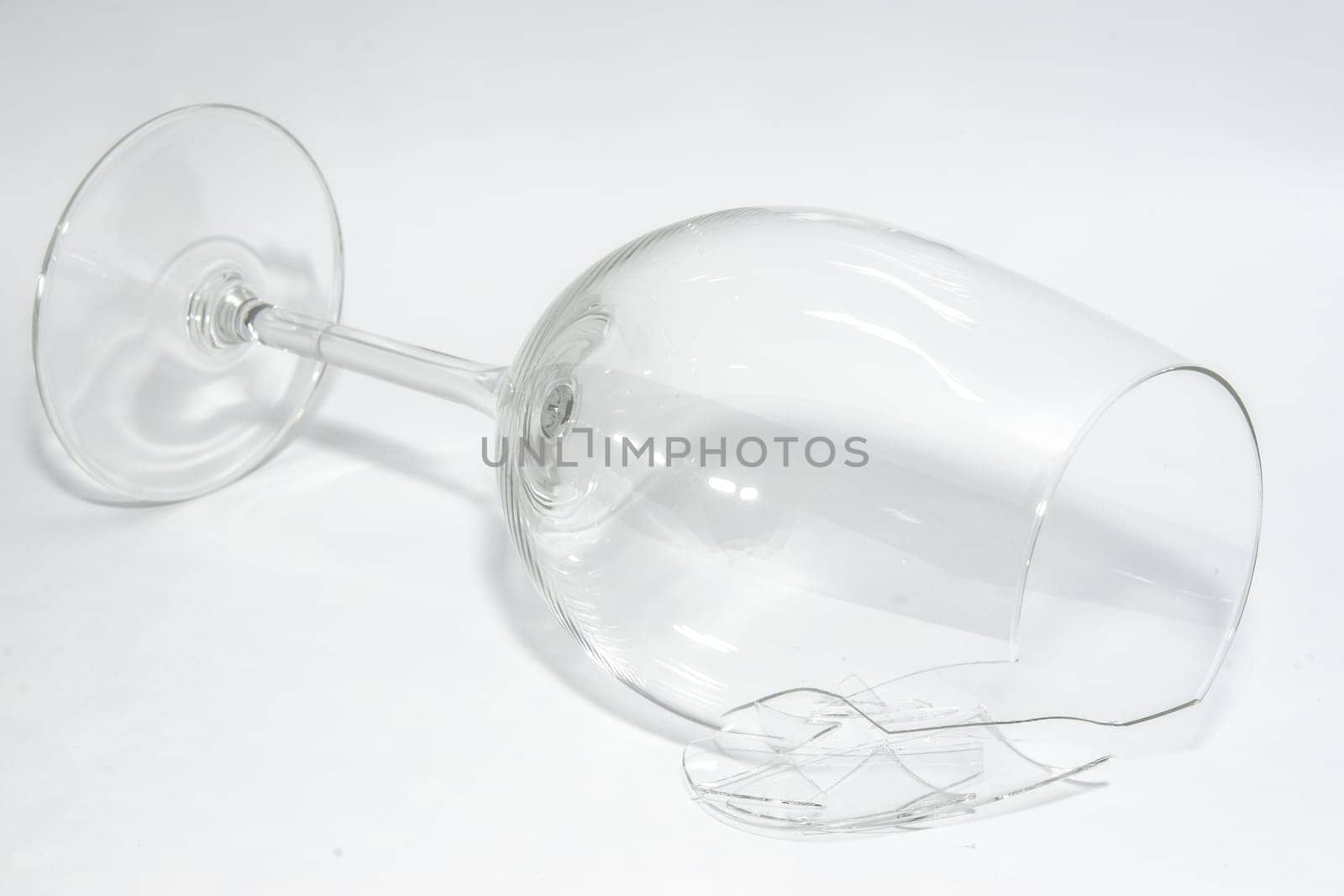 Shattered broken wineglass with sharp splinters lying on white background