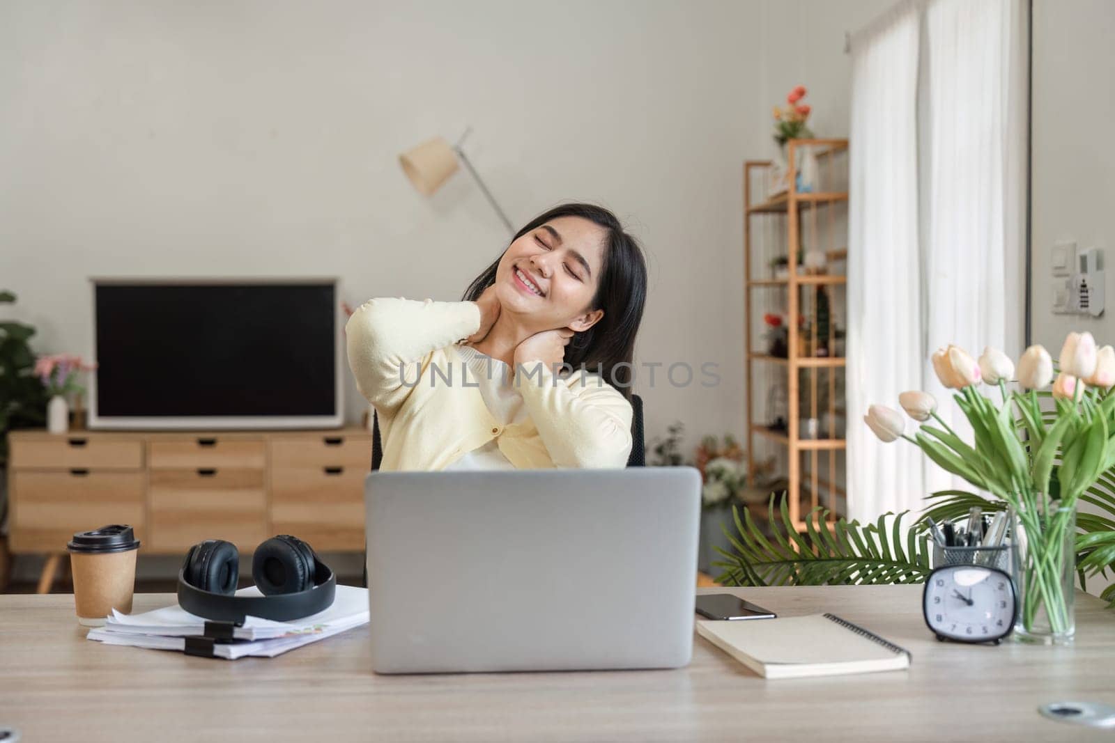 A young woman gently massages her neck while sitting at her desk, showcasing the importance of self-care in a work-from-home setting.