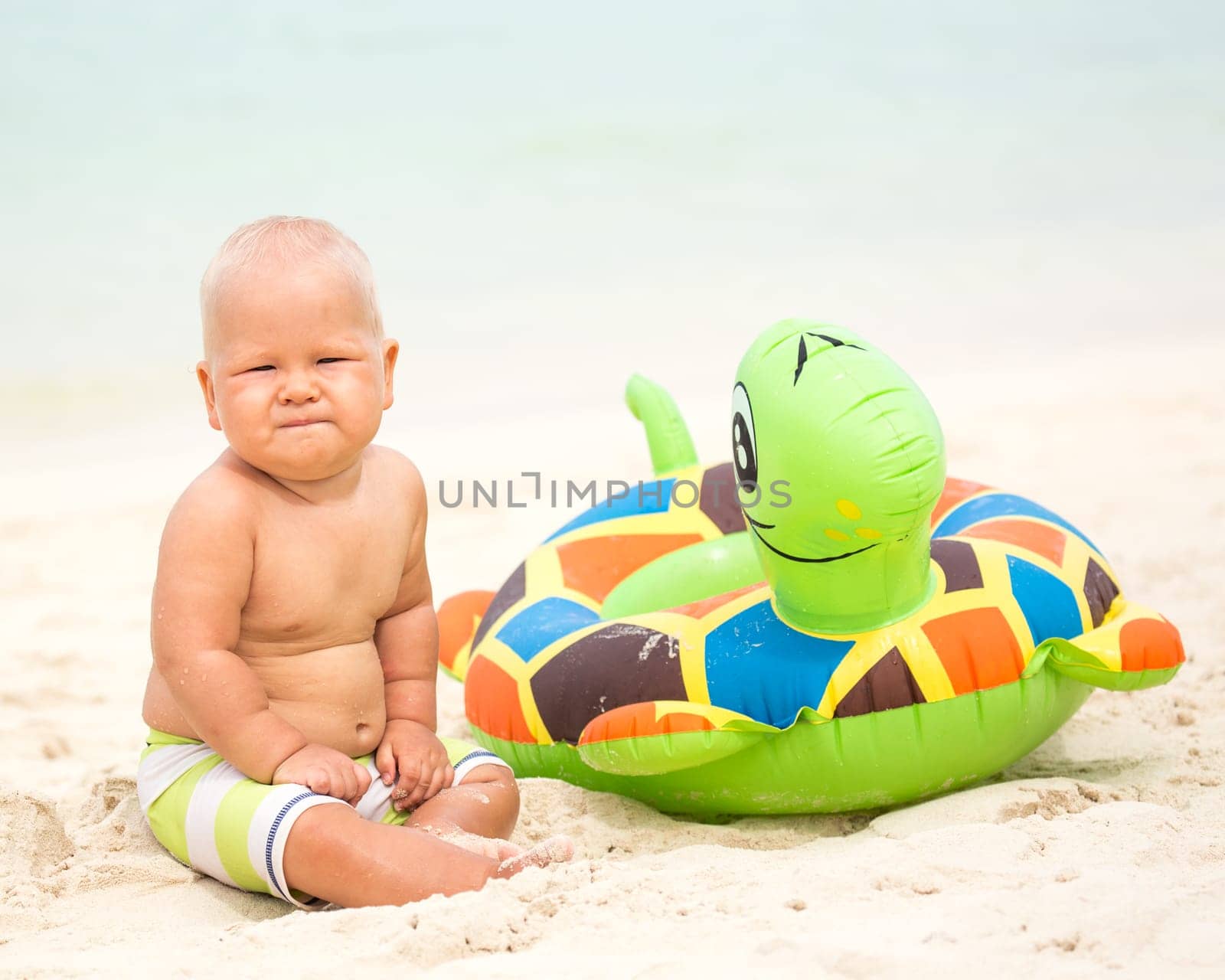 Baby sitting om the beach with swim ring
