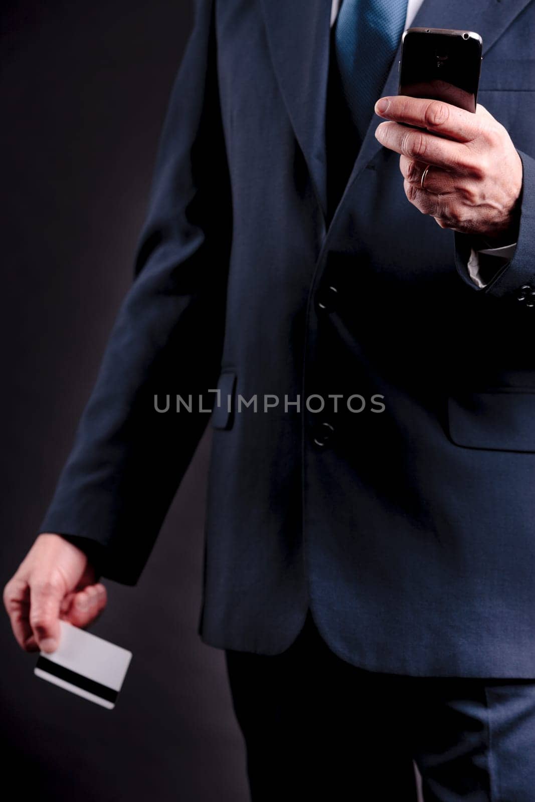 an old businessman with a credit card and a mobile hphone making purchases online  DARK BACKGROUND