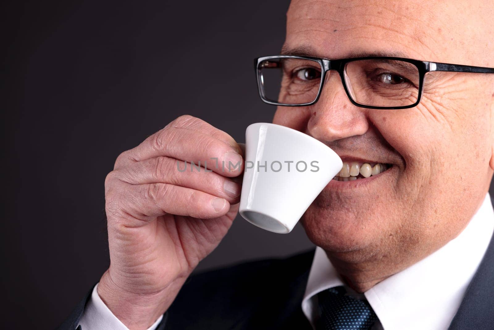 bald old smiling businessman holding a cup of espresso italian coffee