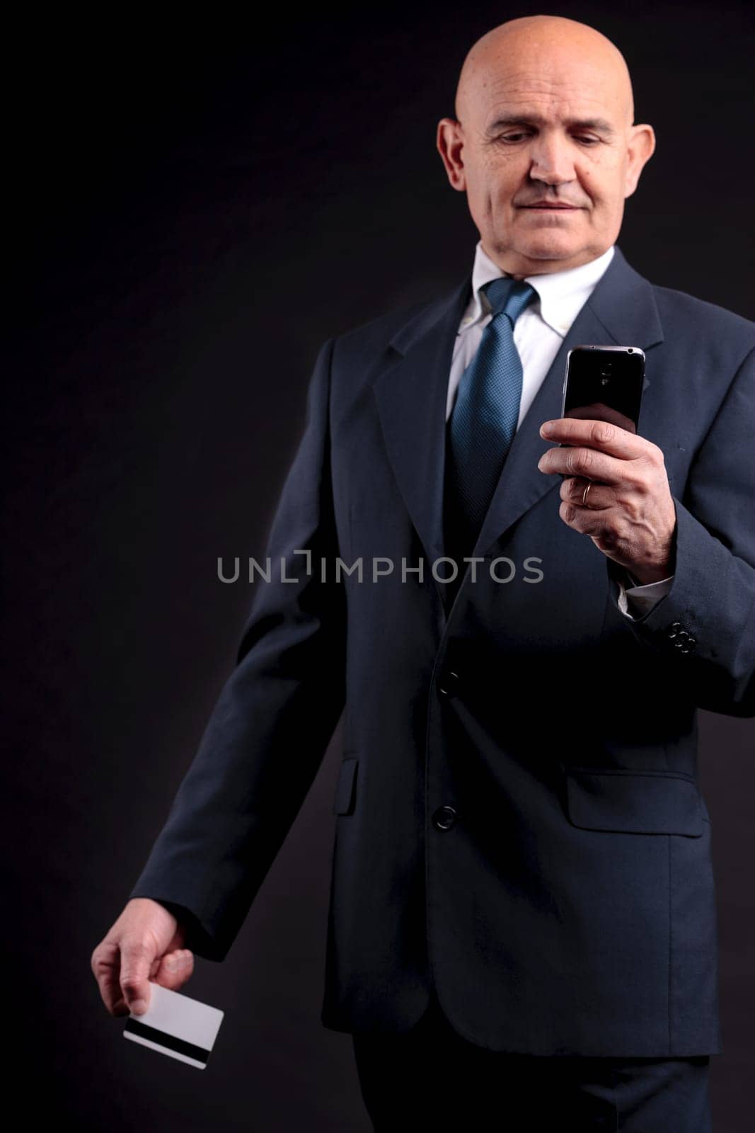 an old businessman with a credit card and a mobile hphone making purchases online  DARK BACKGROUND