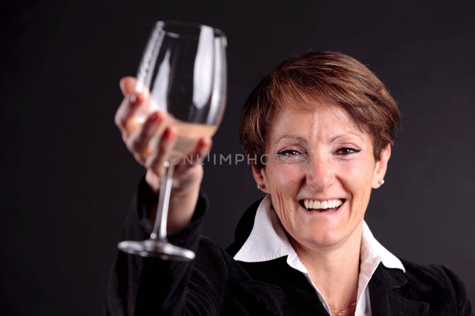 pretty old woman rising up a glass of wine with glaze on camera with focus on face