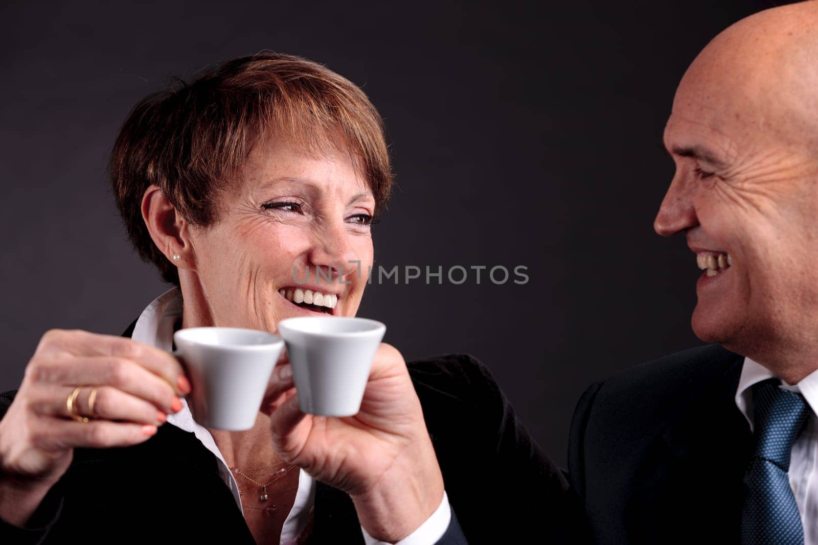 a smiling elderly couple holding up two cups of italian espreso coffee and smiling each other