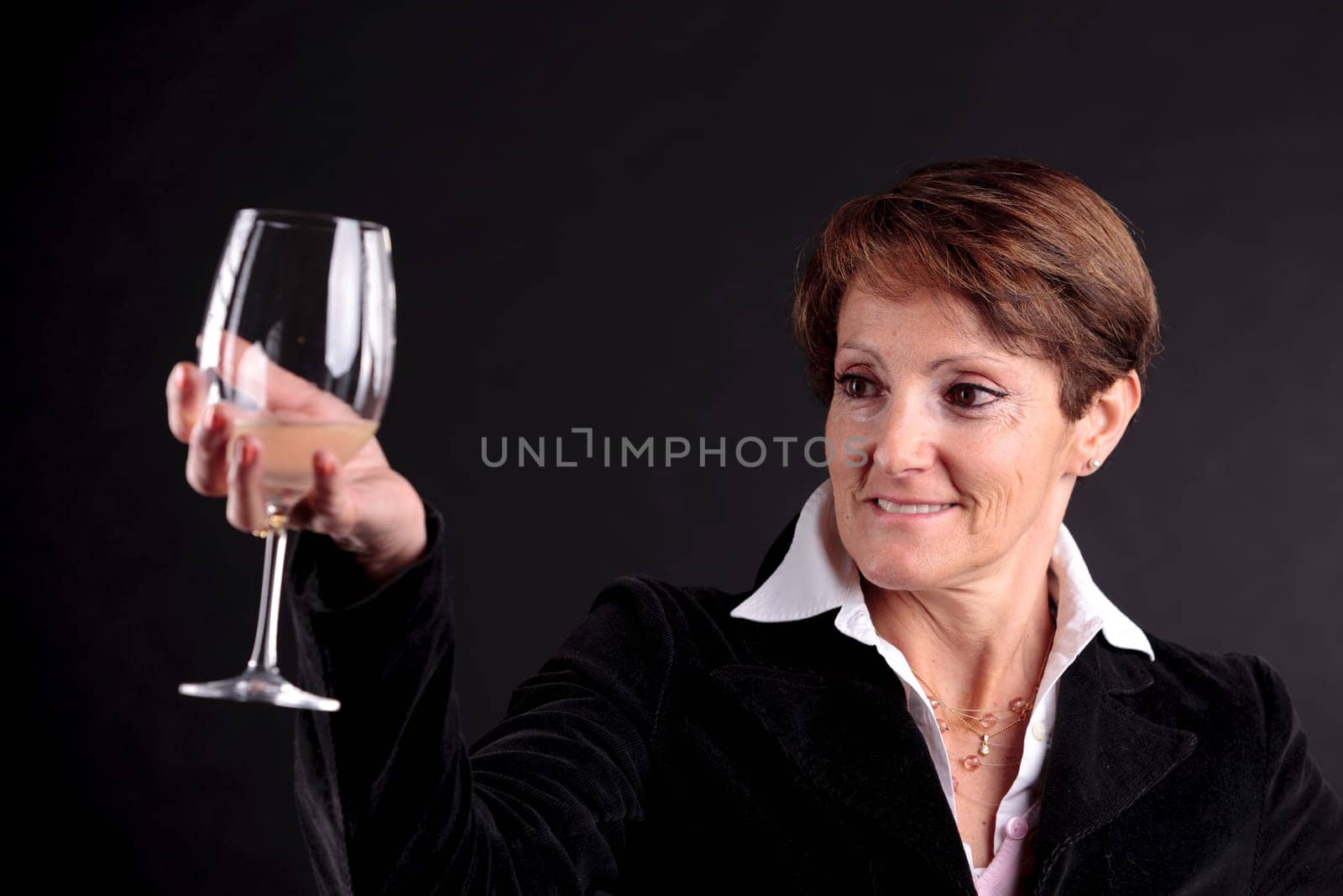 pretty old woman rising up a glass of wine and watching it (focus on the face)