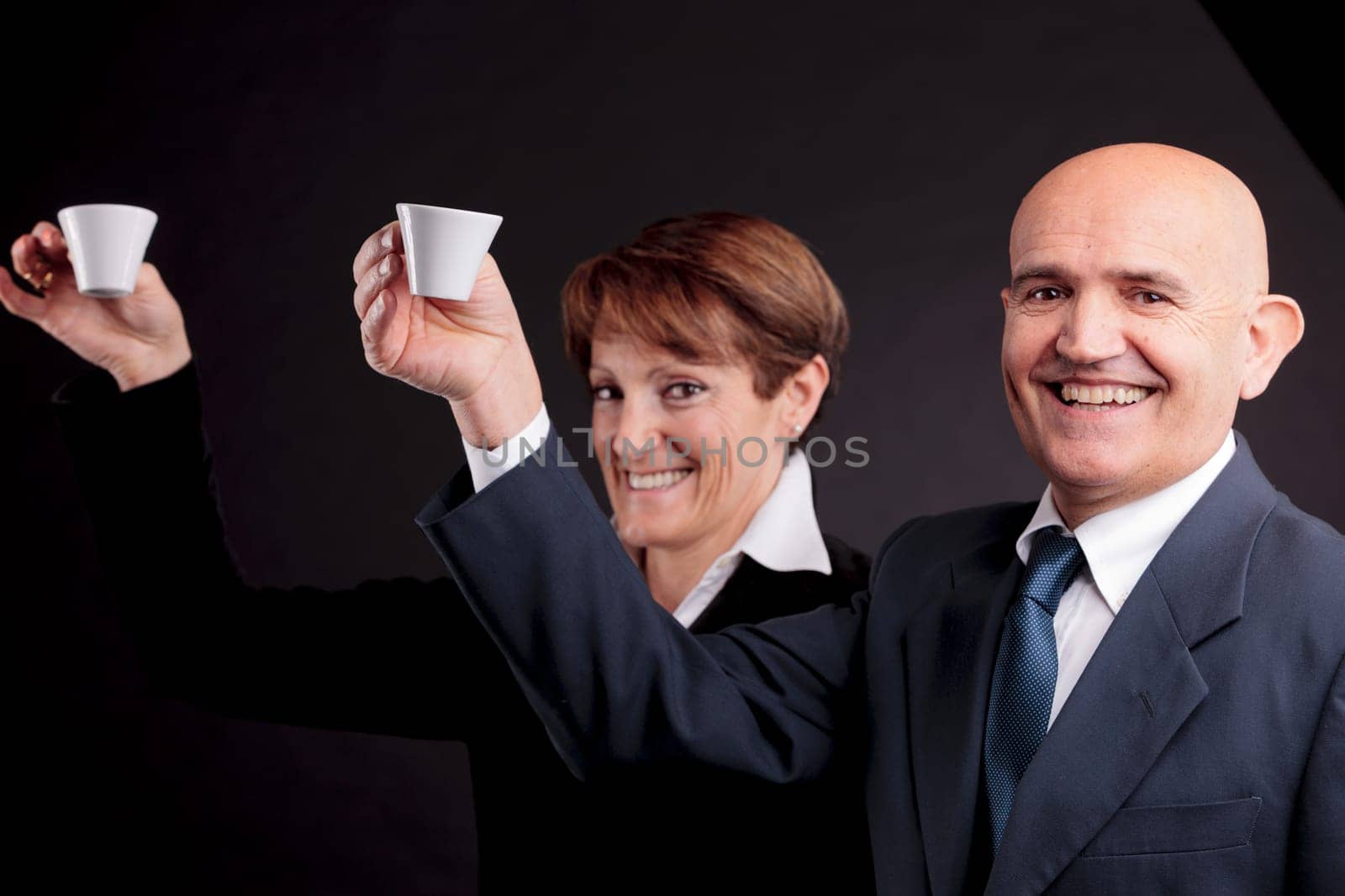 a smiling elderly couple holding up two cups of italian espreso coffee and smiling each other