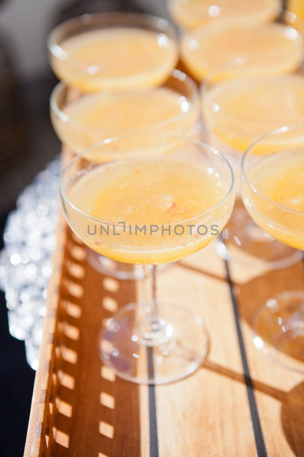 Closeup of glasses of orange juice in rows on wooden serving tray at outdoor party in sunlight