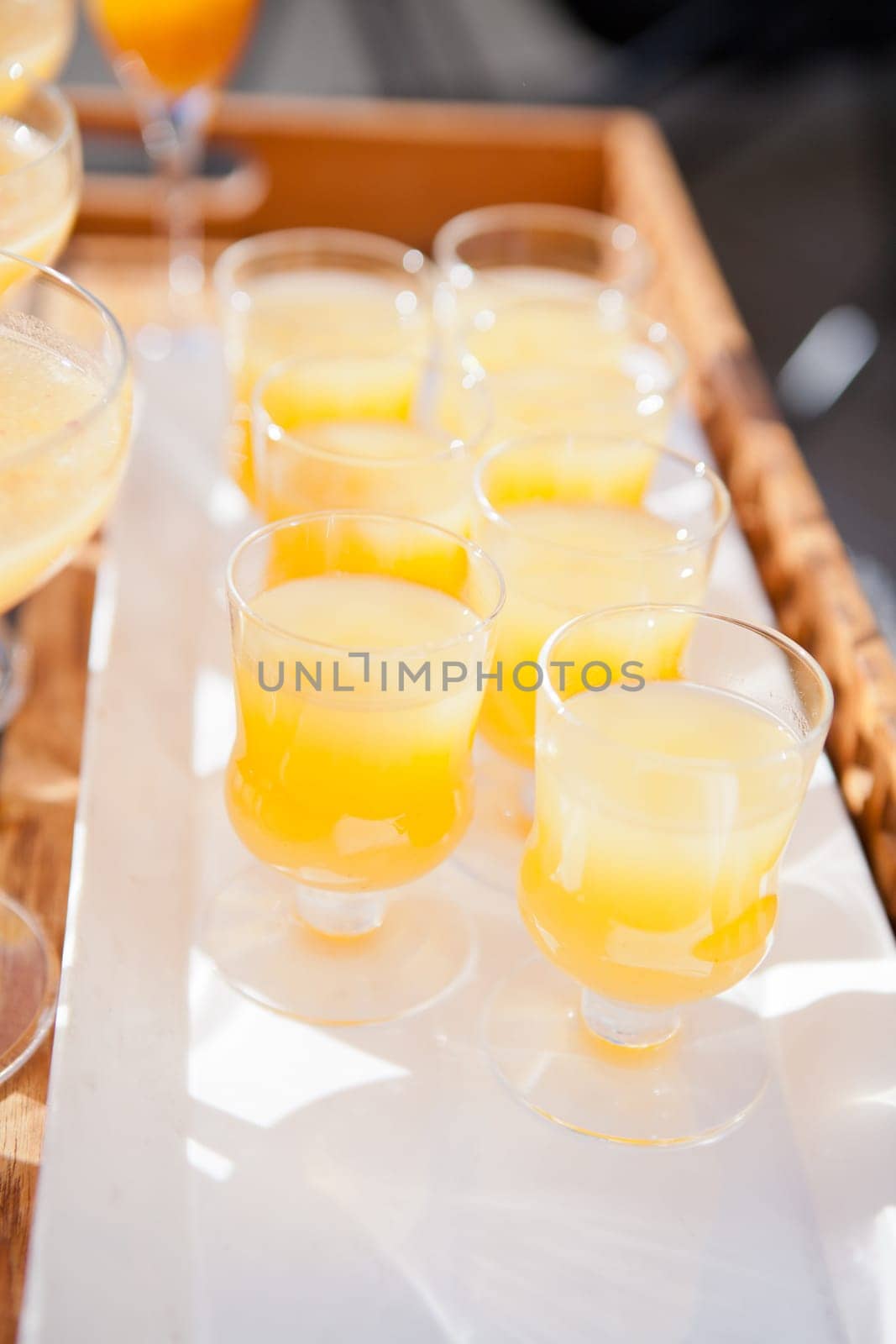 Closeup of glasses of orange juice in rows on serving tray at outdoor party in sunlight