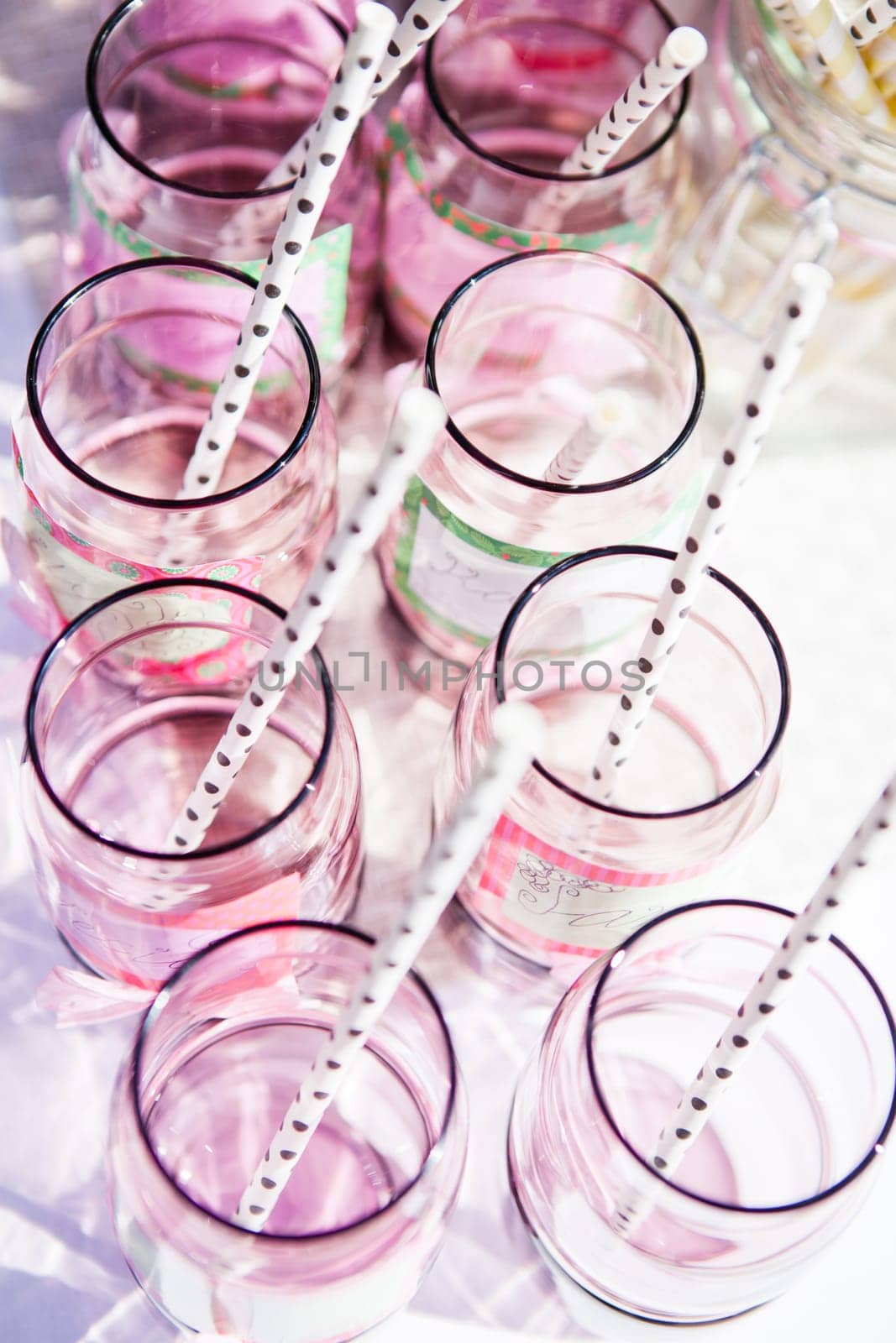 Closeup of decorative pink colored party glasses with straws on table outdoors on bright day