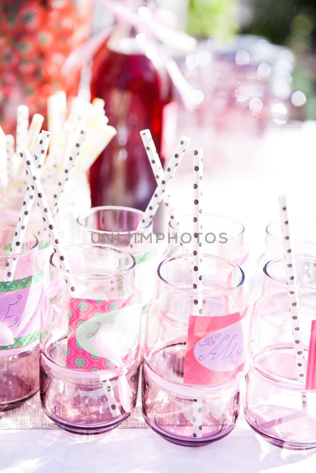 Closeup of decorative pink colored party glasses with straws on table outdoors with bottle of fruit juice in background