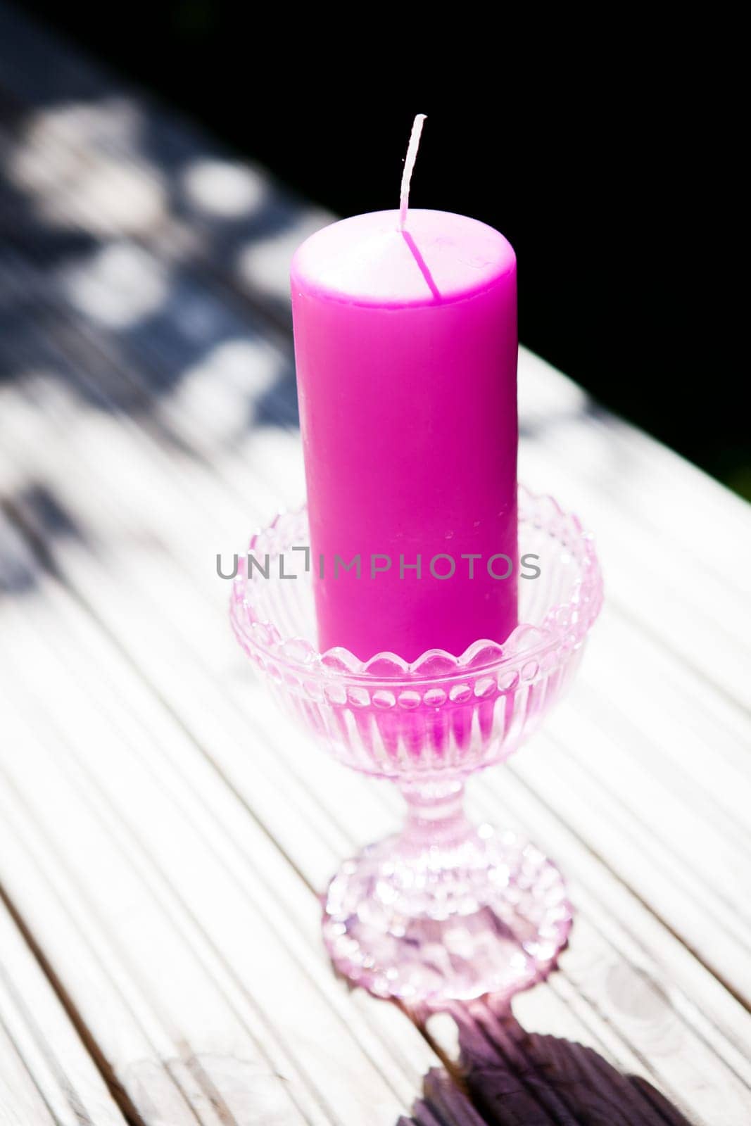 Closeup of decorative purple candle in glass stand resting on table outdoors on sunny day