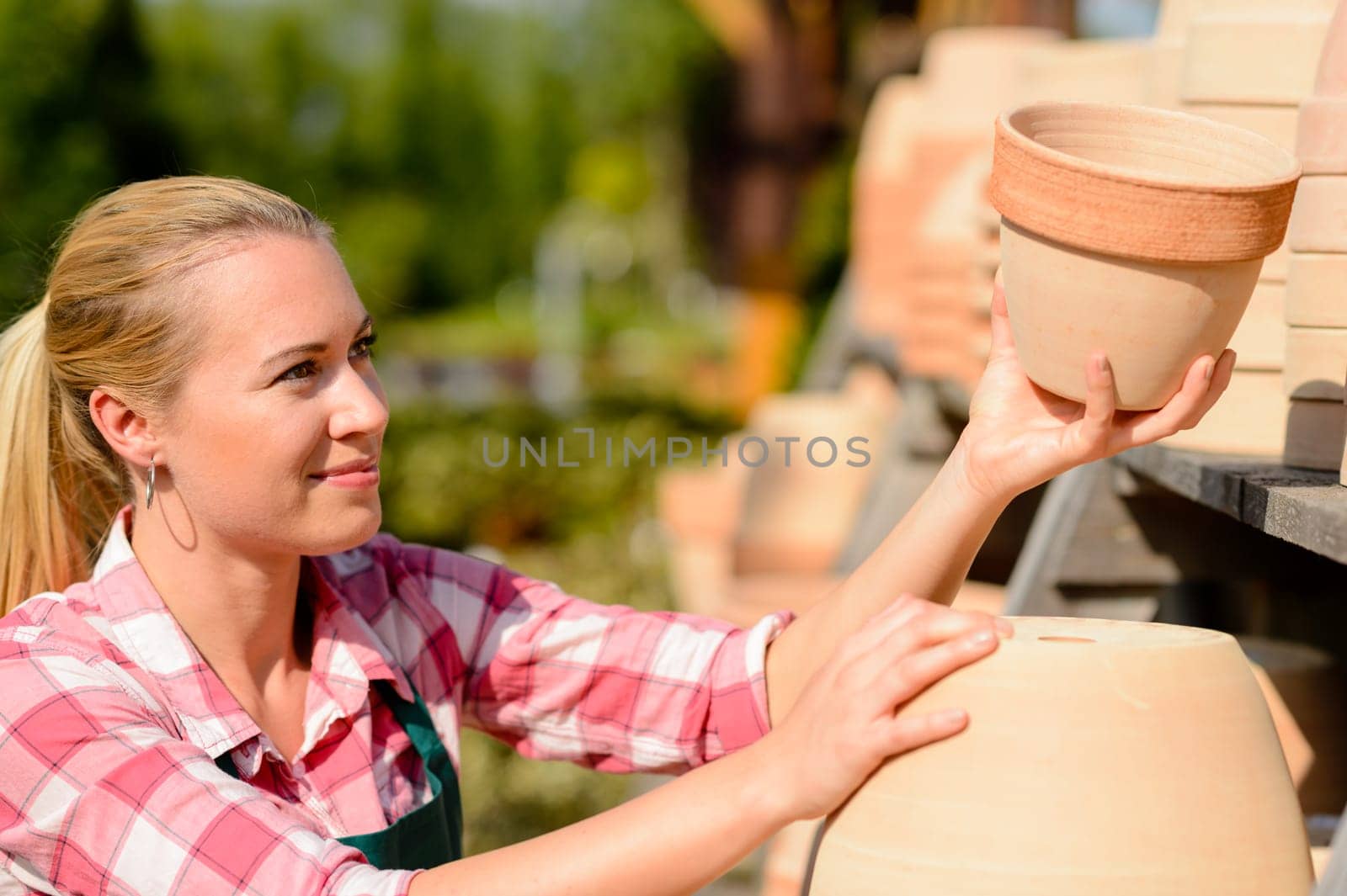 Garden center woman worker putting clay pots on shelf sunny