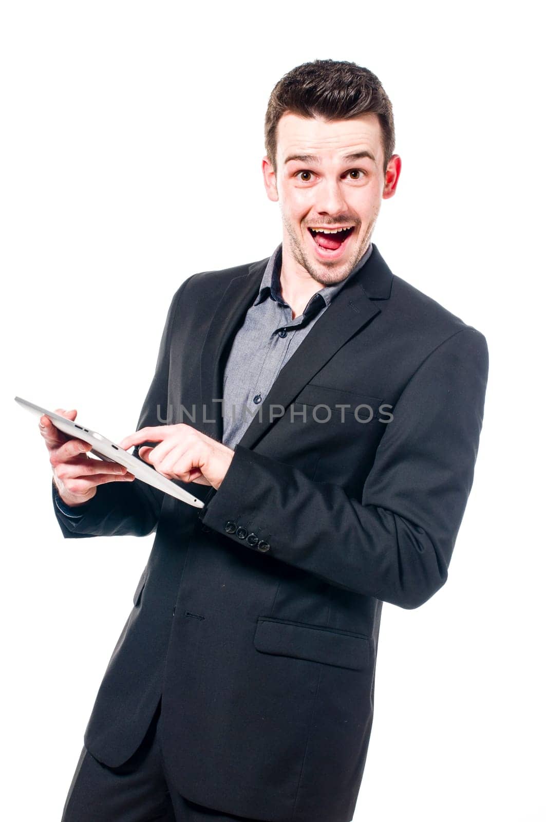 Young businessman in suit typing on a tablet computer and laughing at the camera, isolated on white.