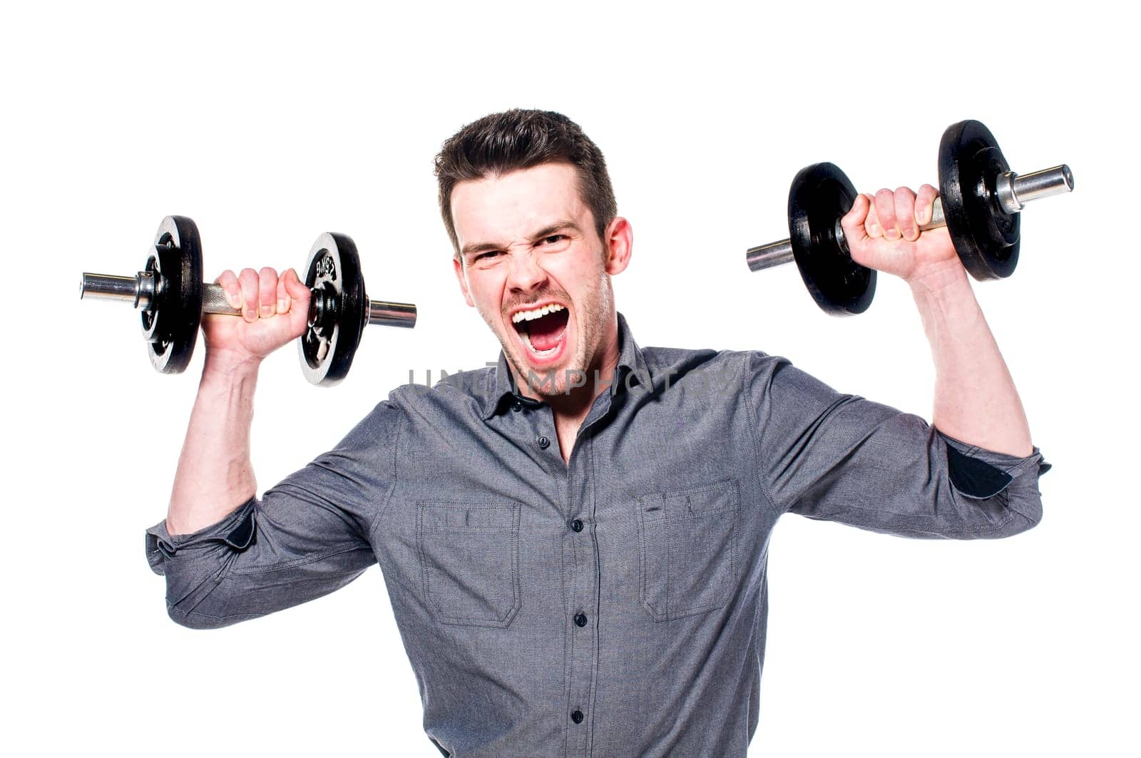 Young male businessman in light suit with power lifts a dumbbell and shows strength and determination, isolated against white background