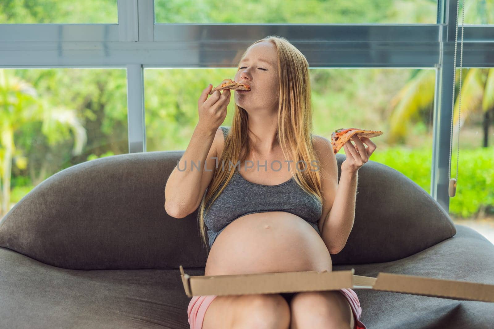 A pregnant woman enjoys a slice of pizza, savoring a moment of indulgence while satisfying her craving for a delightful, comforting treat. Excited Pregnant Young Lady Enjoying Pizza Holding Biting Tasty Slice Posing With Carton Box. Junk Food Lover Eating Italian Pizza. Unhealthy Nutrition Cheat Meal by galitskaya